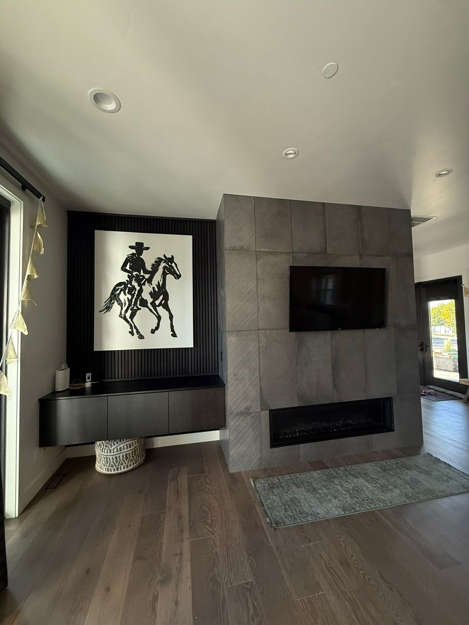 Living room with modern fireplace and art. Dark wood floors, gray fireplace, cowboy art.