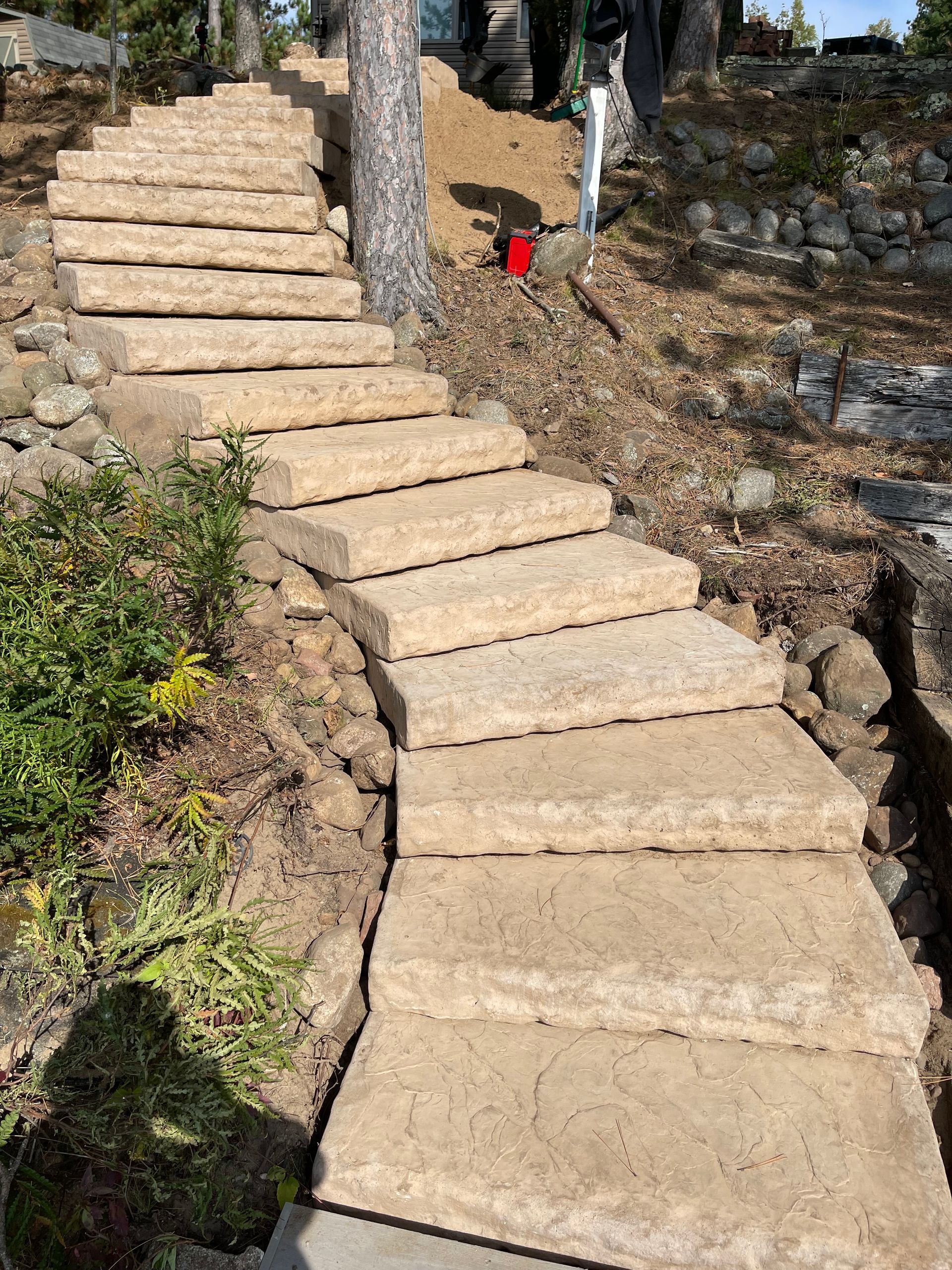 Stone steps leading uphill through a wooded area. Beige stones, dirt, and some vegetation.