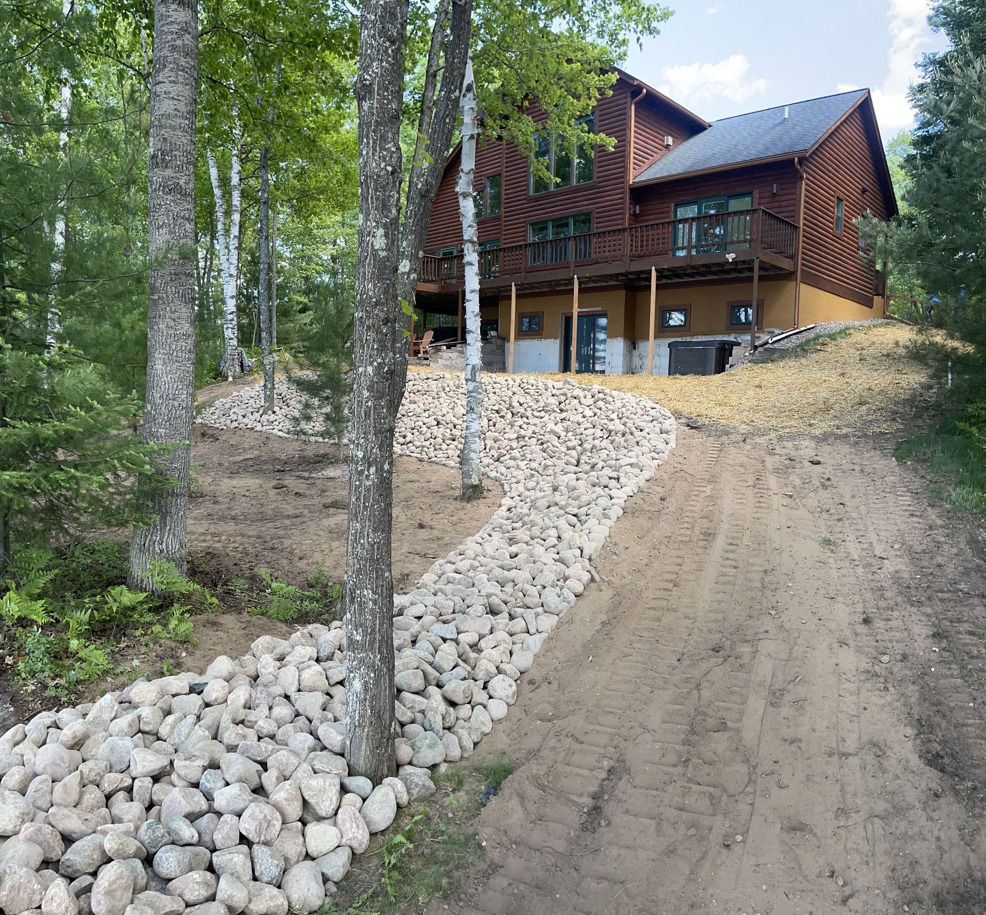 A two-story brown house on a hill with a gravel path winding up. Trees flank the path.