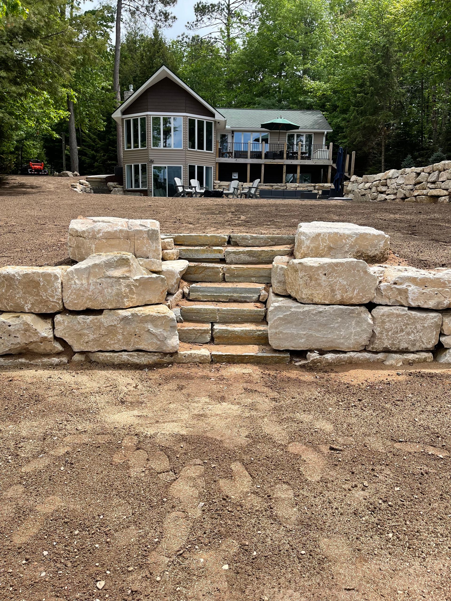 Stone steps lead up to a two-story house with a lake view, set in a natural landscape.