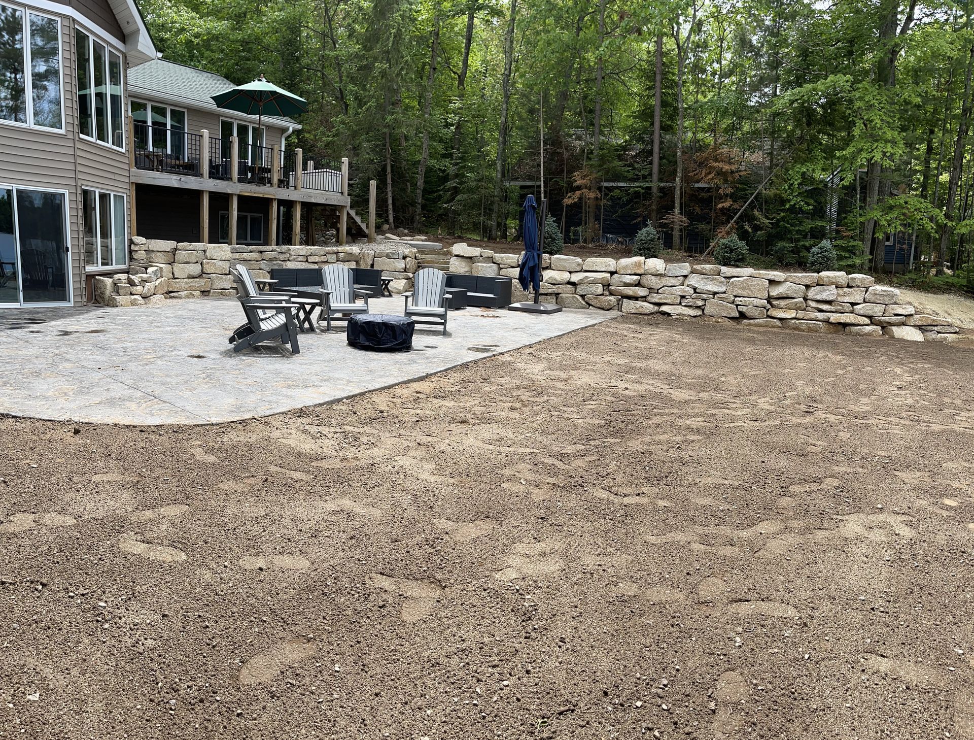 Outdoor patio with gravel seating area and retaining wall in a wooded setting.