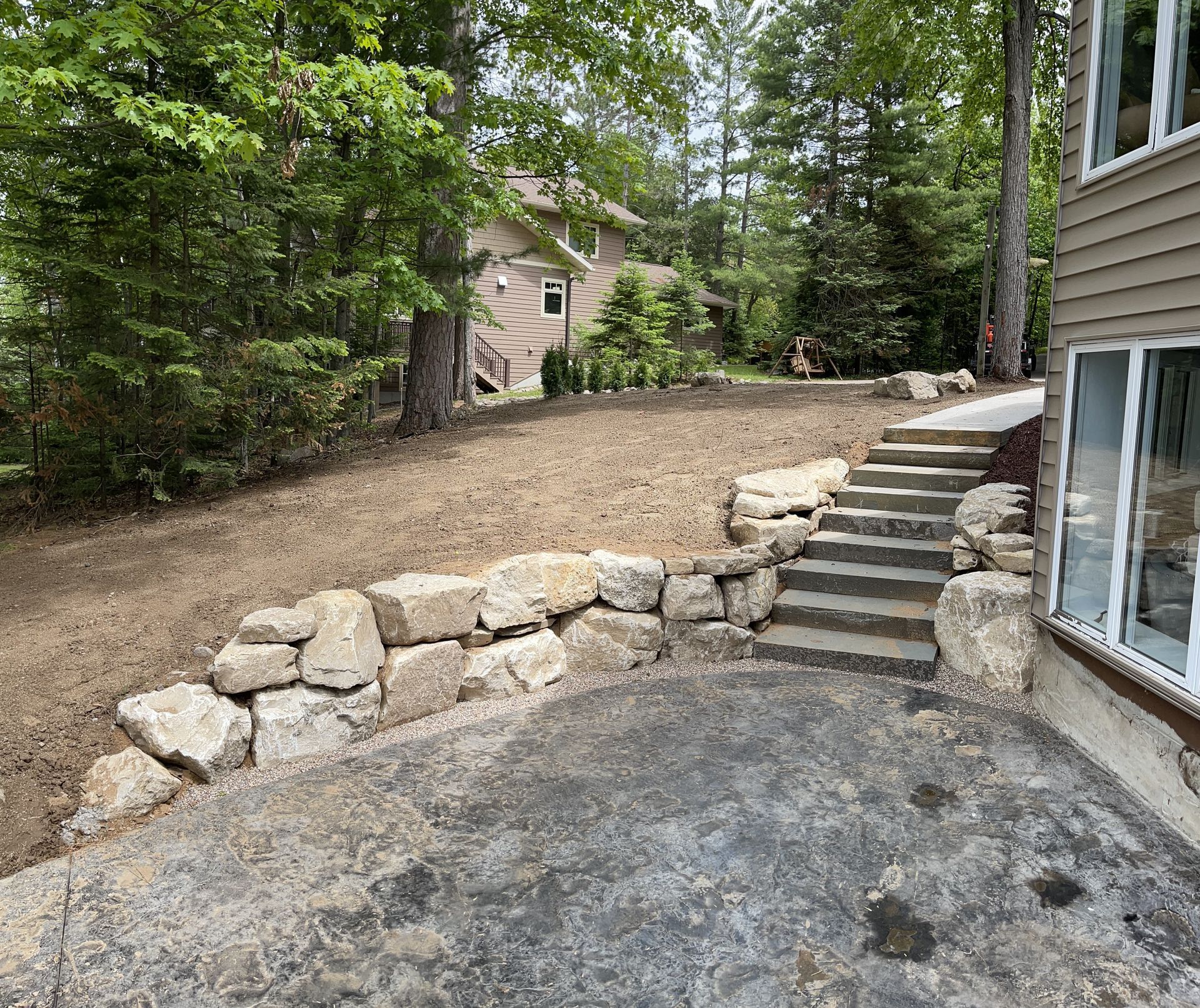 Stone retaining wall with steps leading up to a grassy area, a house visible in the background.