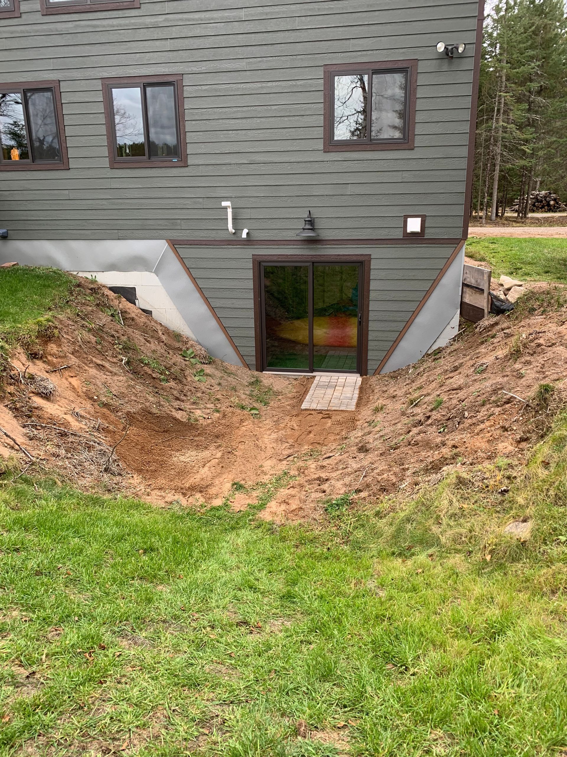Exterior view of a house with a sunken entryway. A kayak is visible inside the glass doors. Earth surrounds the entrance.