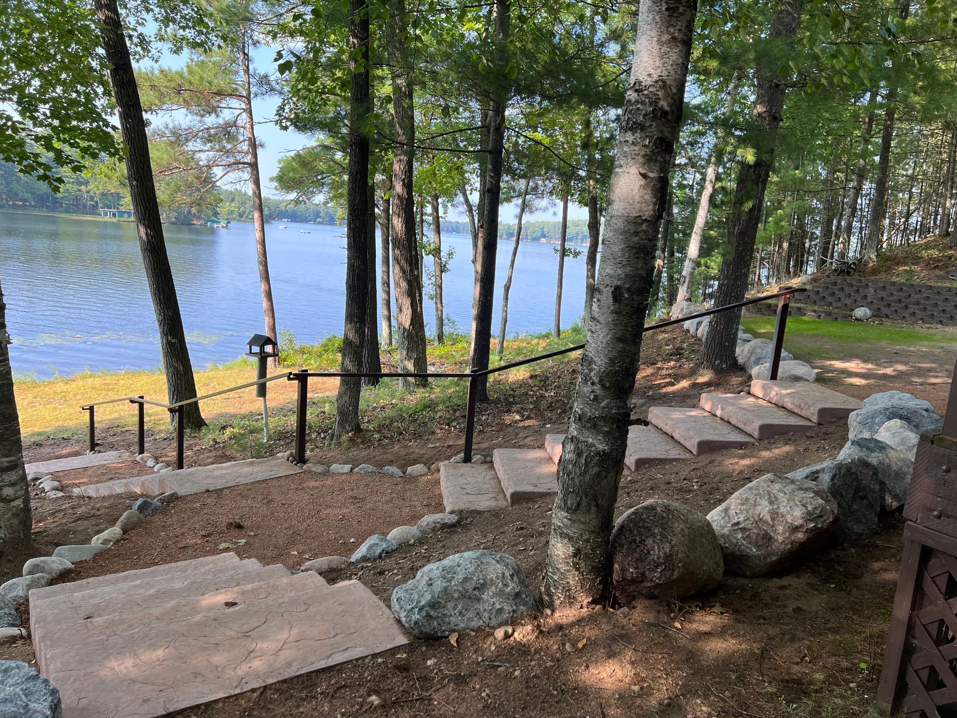 Stone steps lead to a lake, flanked by trees and a black handrail.