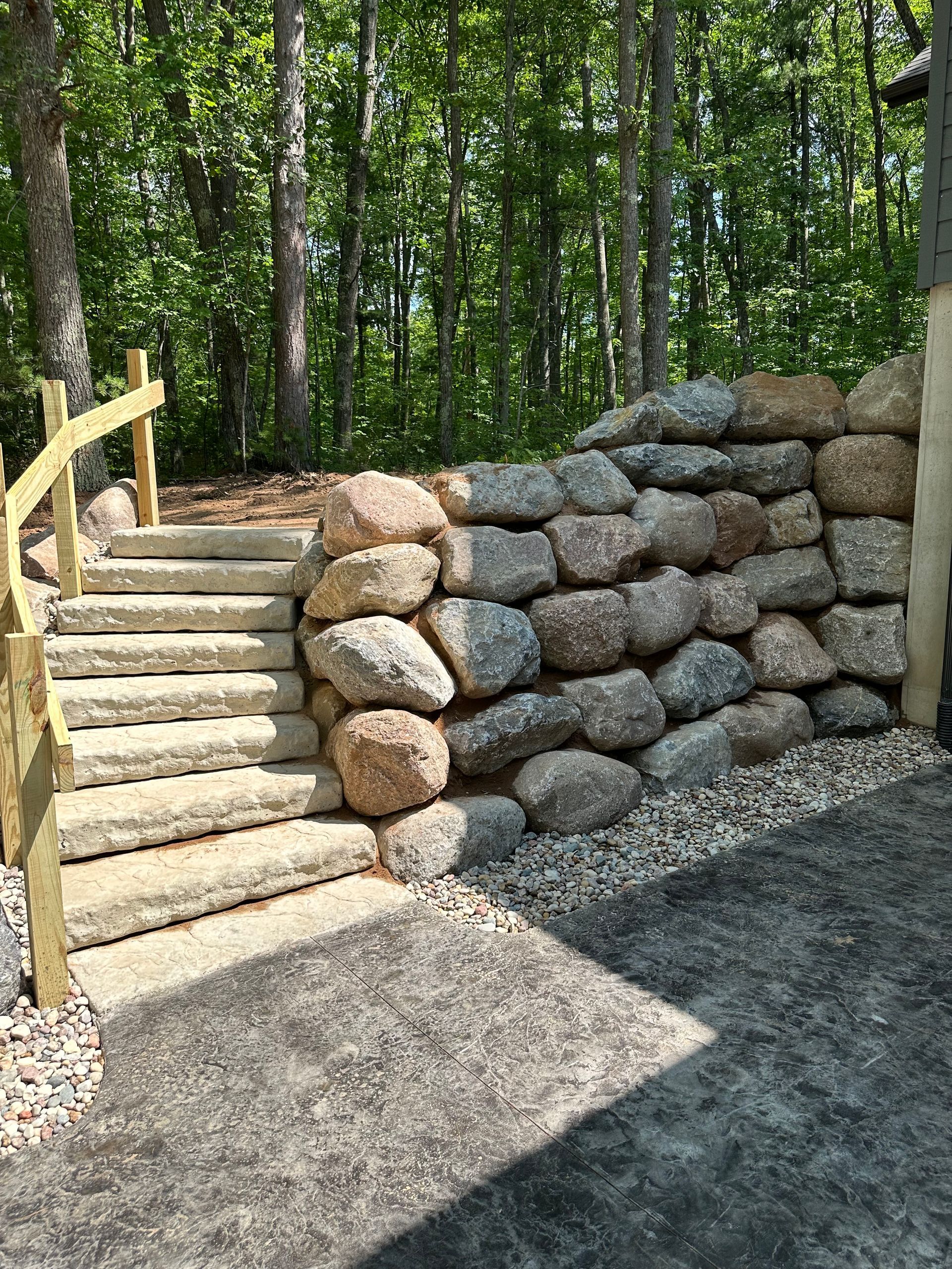 Stone steps and wall alongside a wooden handrail, leading up into a forest.