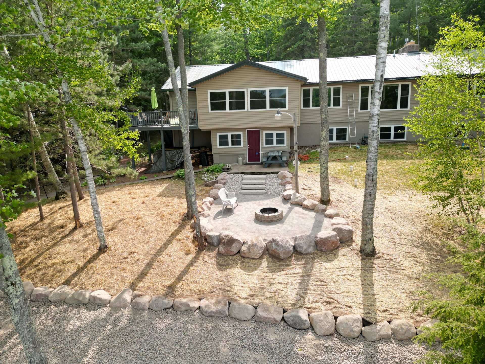 Two-story tan house with a fire pit, surrounded by birch trees. Exterior view on a sunny day.