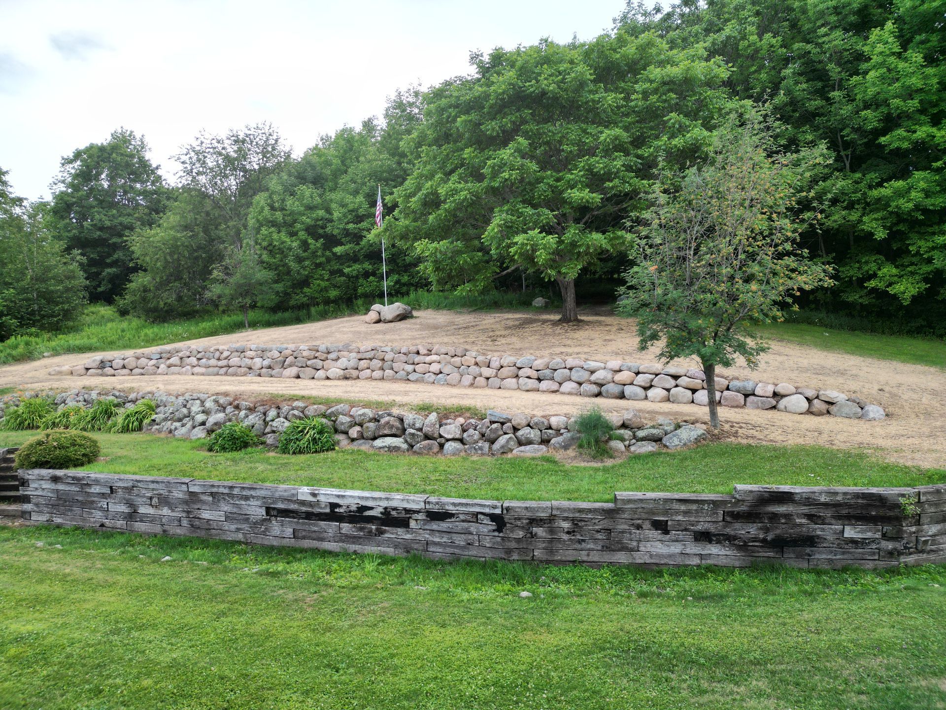 Stone terraces and walls on a grassy hillside, with trees and a flag pole in the background.