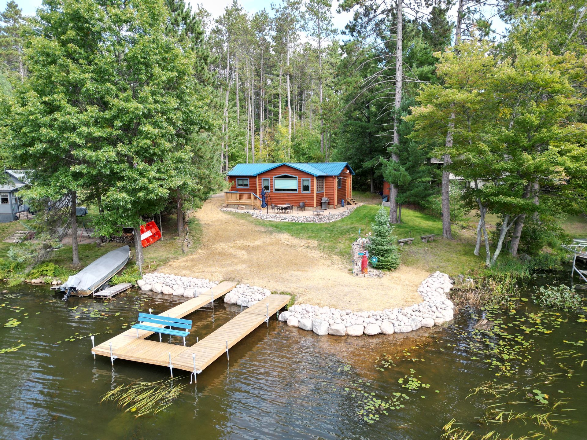 Cabin on a lake with a dock, small beach, and surrounding trees.