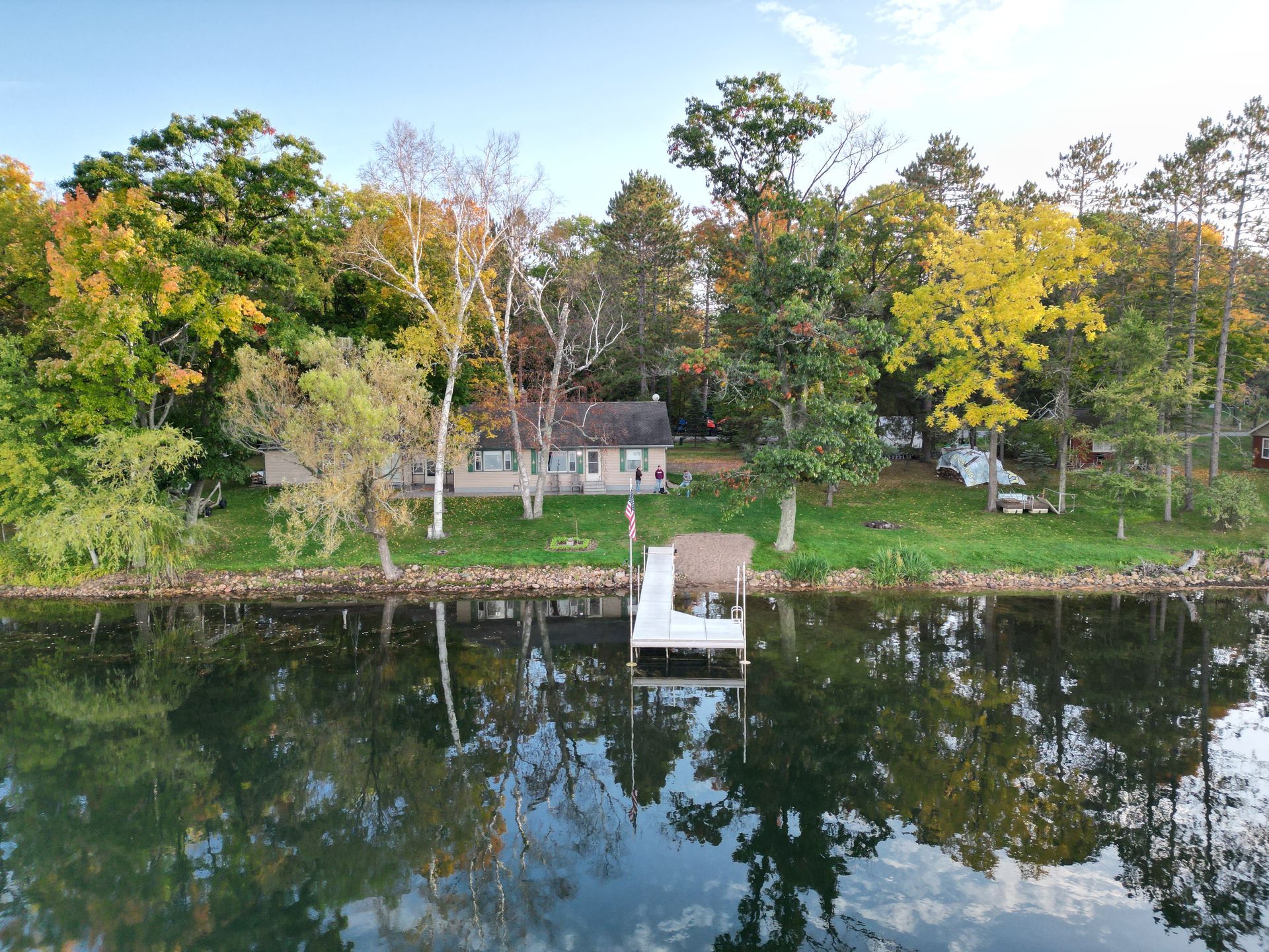 Lakeside house with white dock and colorful trees reflecting in the water.