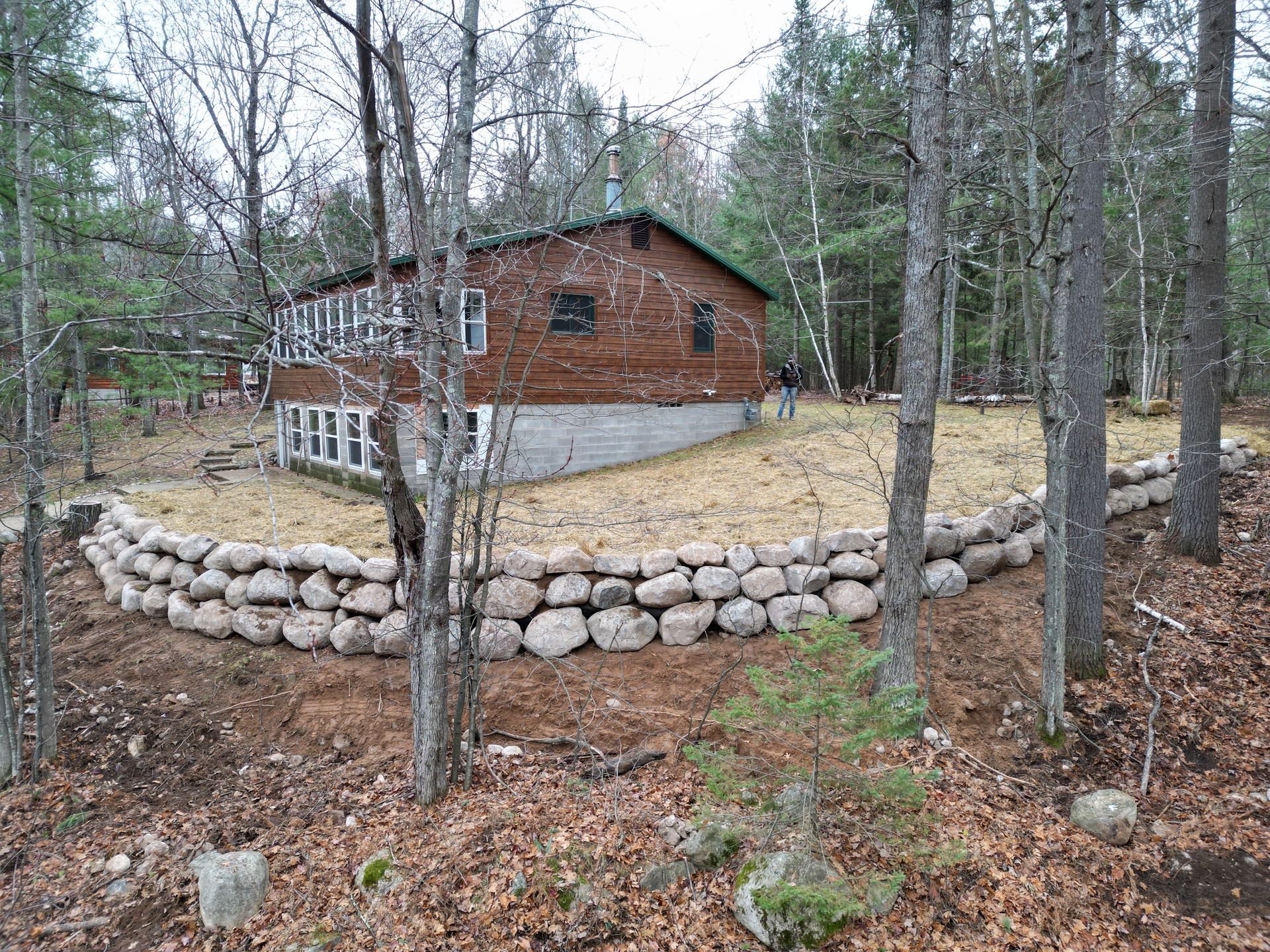 Brown house nestled in a forest, surrounded by a stone wall.