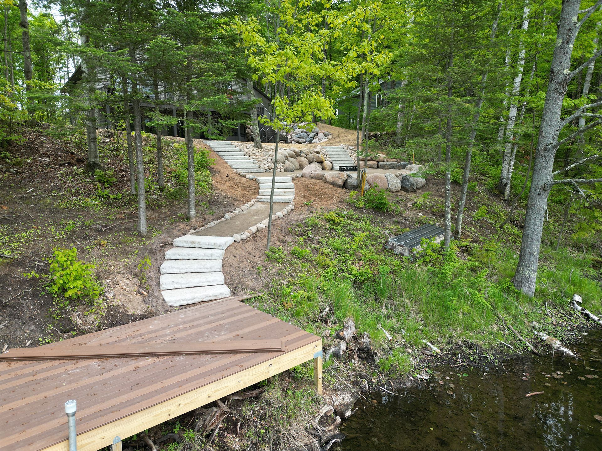 Wooden dock leads to stone steps up a wooded hillside, near a body of water.