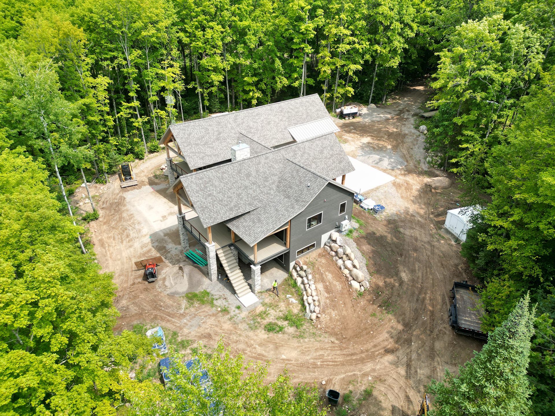 Aerial view of a gray-roofed house under construction surrounded by a wooded area.