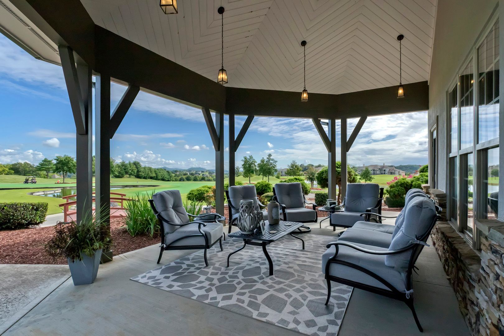 Outdoor patio with seating, overlooking a golf course, under a covered structure with hanging lights.
