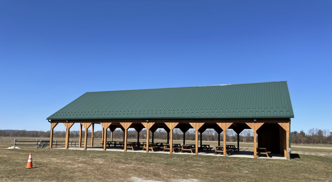 A large pavilion with a green roof is sitting in the middle of a field.