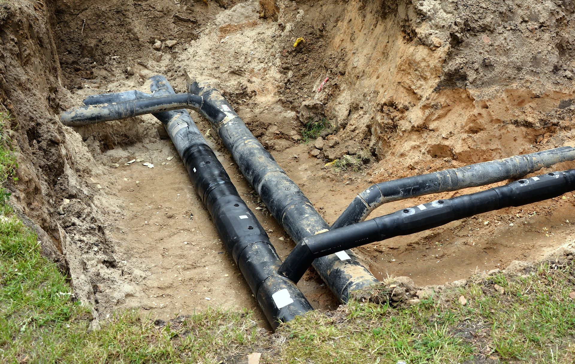 Black pipes in a dirt trench, likely underground utilities, next to grass.