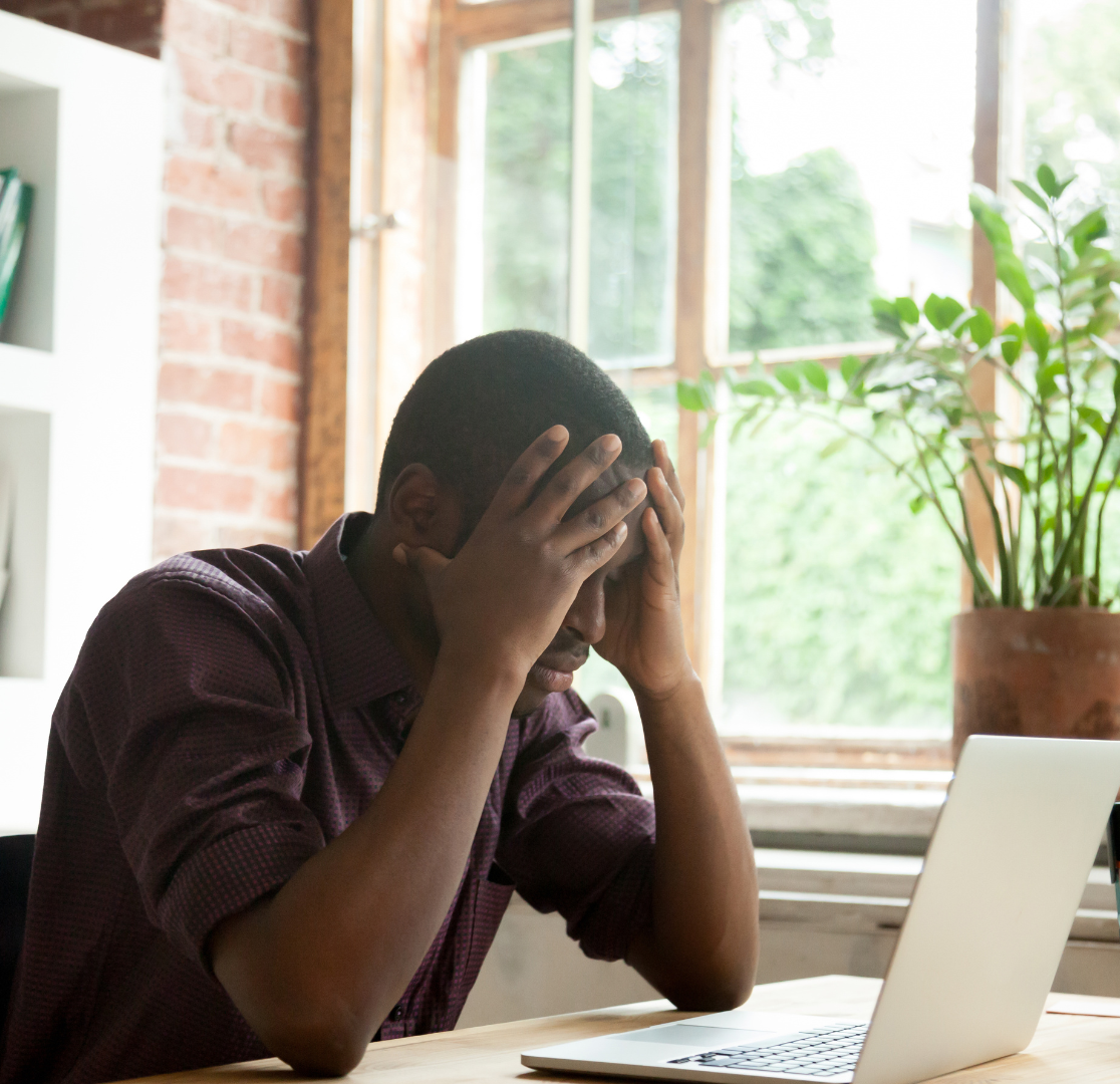 Frustrated property owner sitting at a desk, looking at paperwork and a laptop while trying to plan property management tasks.