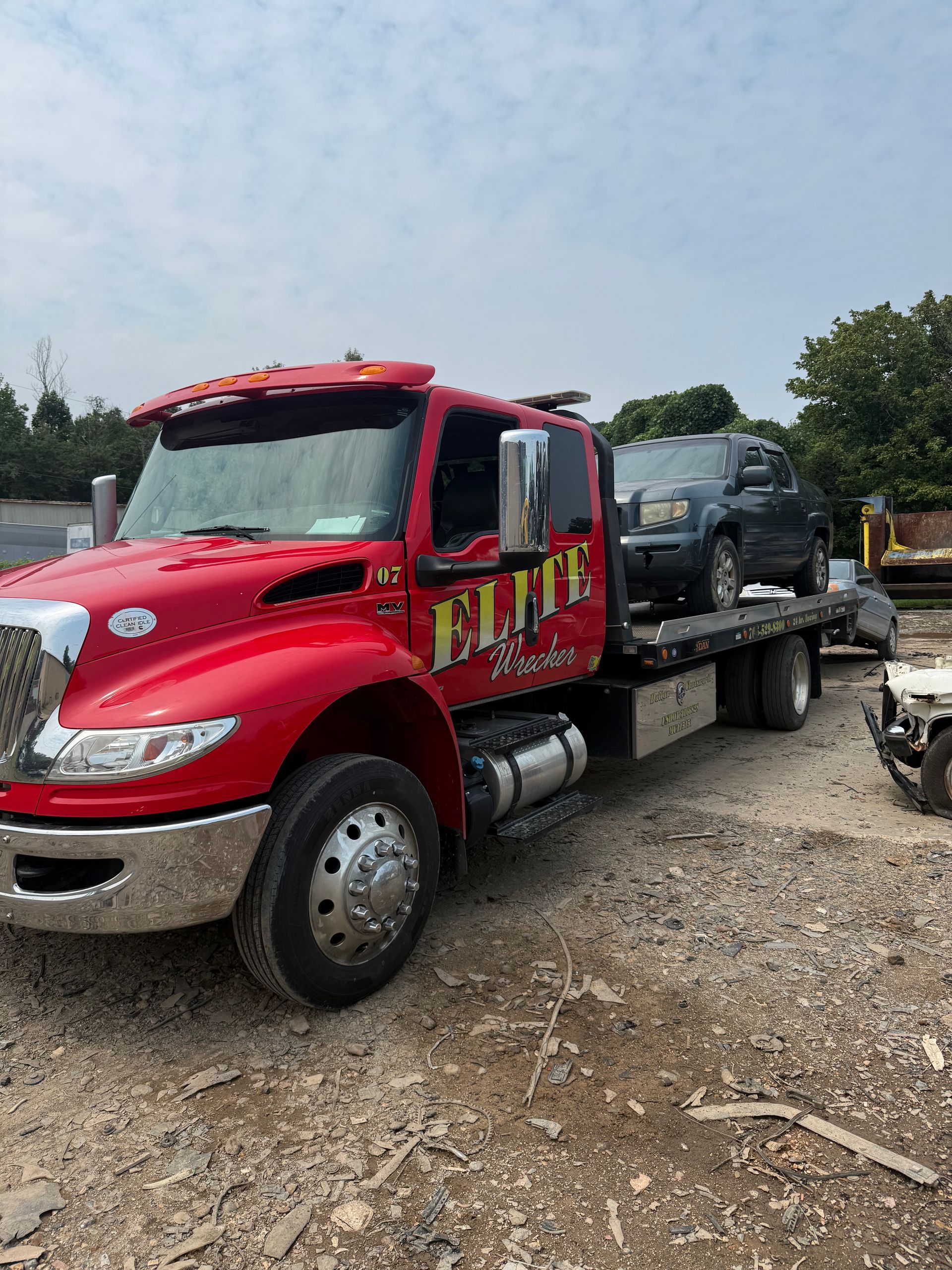 Red tow truck carrying a dark gray SUV on a flatbed in a gravel lot