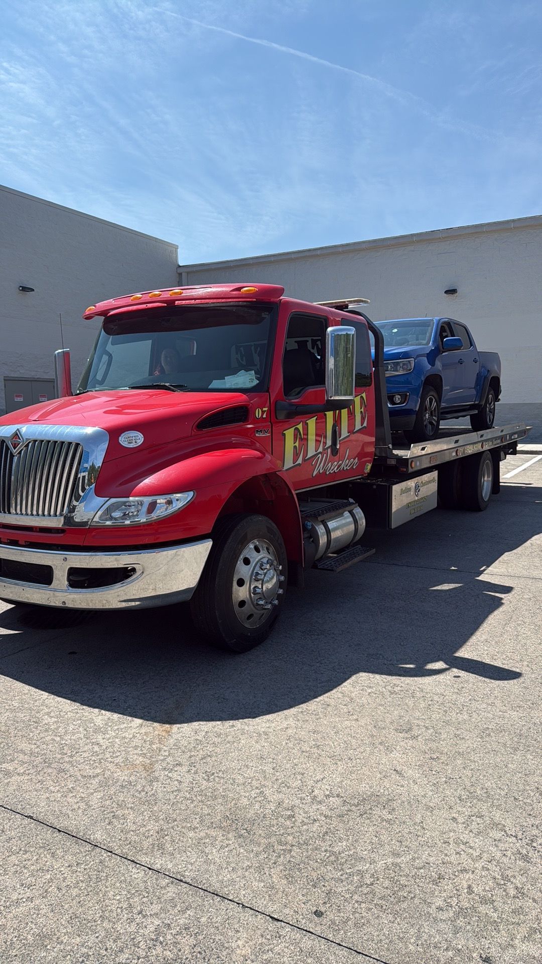 Red flatbed tow truck carrying a blue pickup in a parking lot