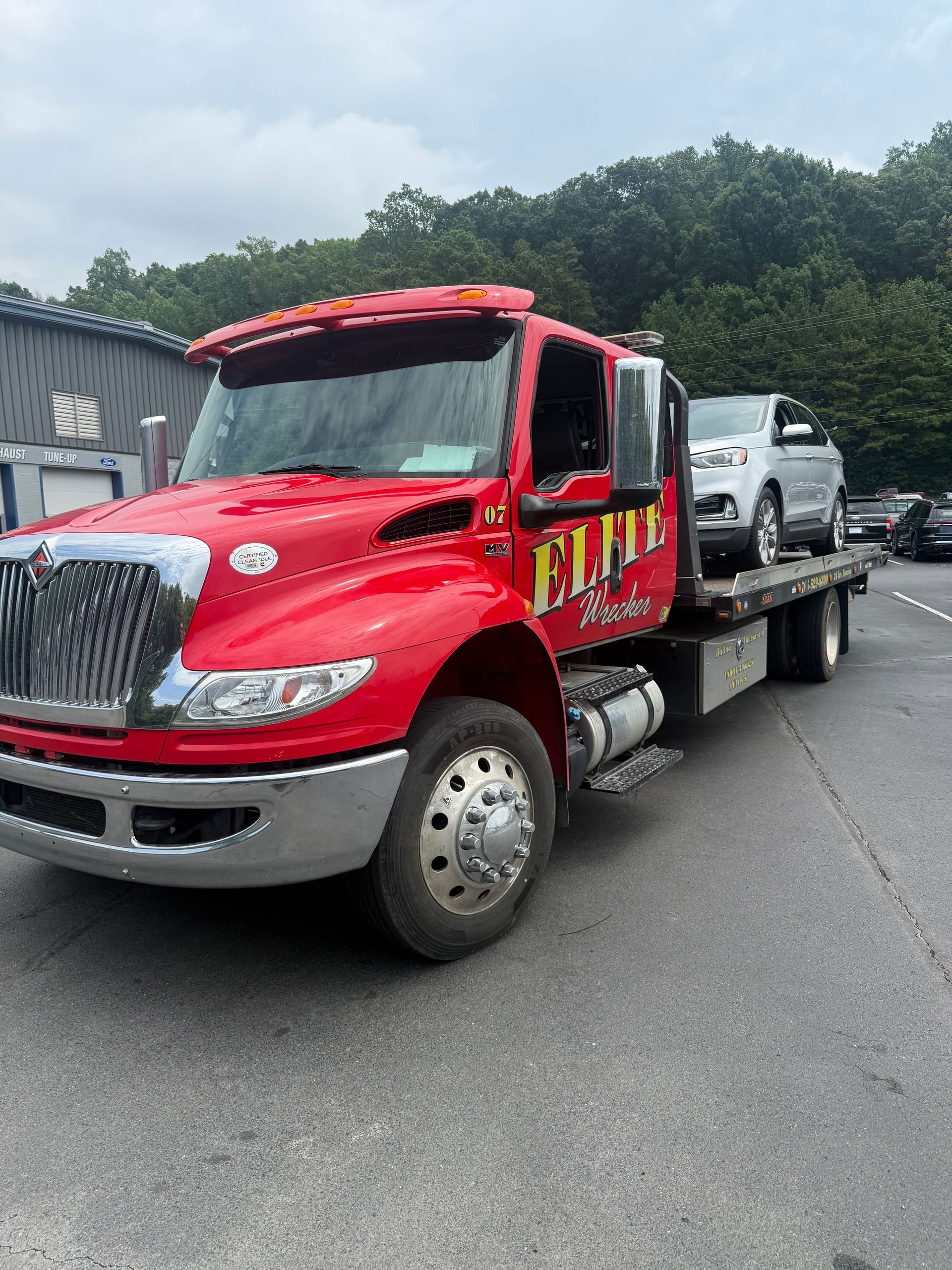 Red flatbed tow truck hauling a silver SUV on a roadside near trees and buildings.