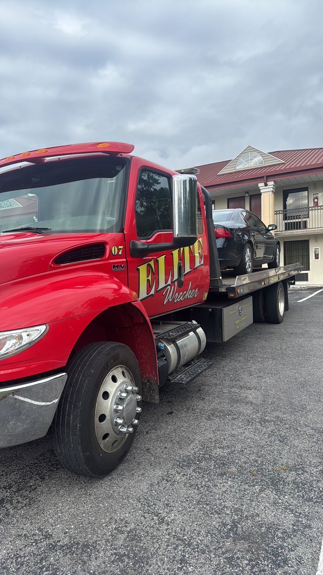 Red flatbed tow truck parked on a gravel lot under a cloudy sky