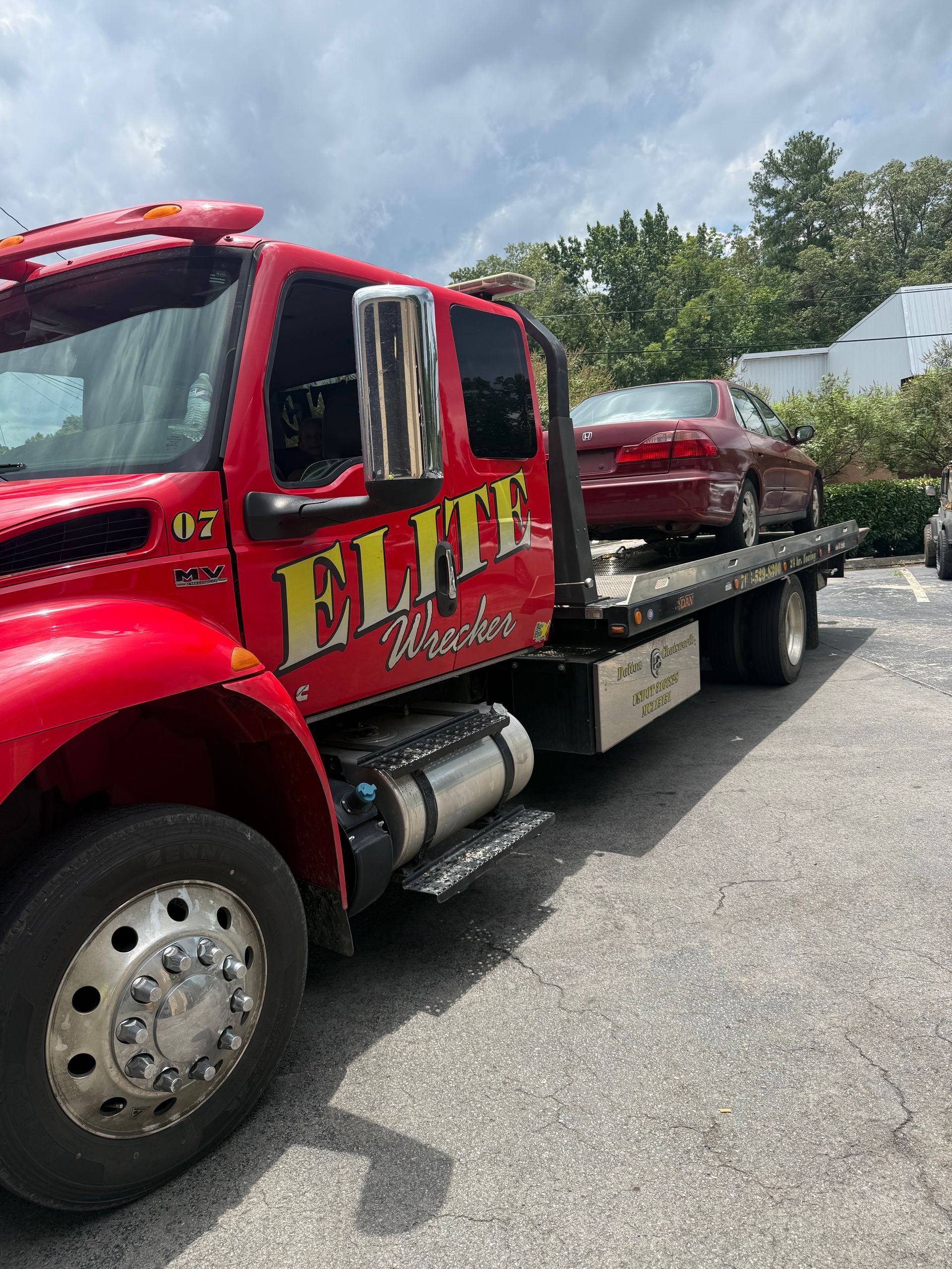 Red flatbed tow truck carrying a red car on a roadway under cloudy skies