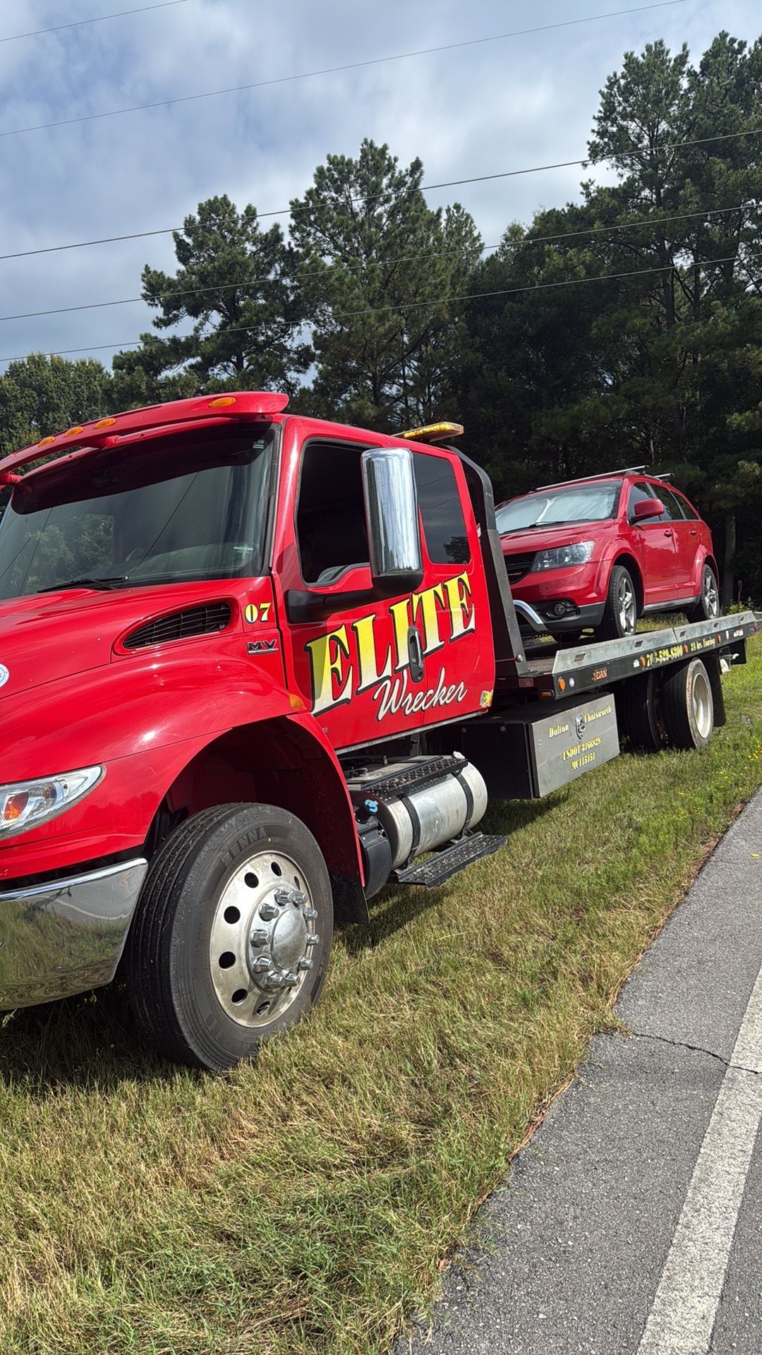 Red tow truck carrying a red sports car on a flatbed beside a road