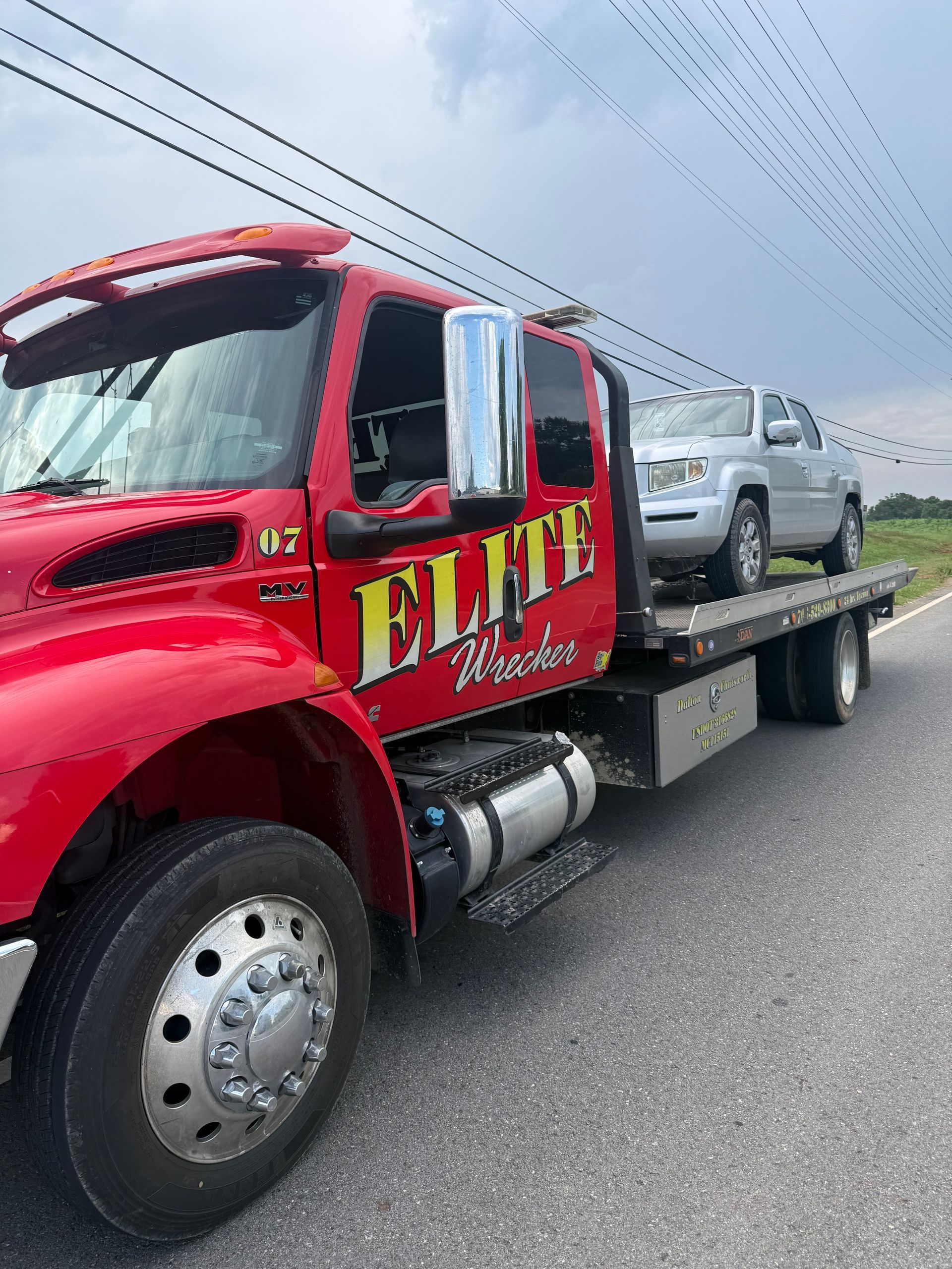 Red Elite towing flatbed truck hauling a silver SUV on a highway