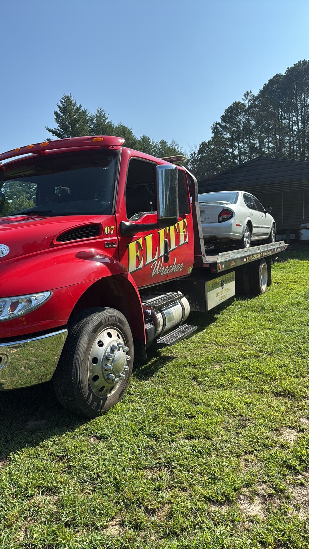 Red tow truck carrying a white SUV on a flatbed in a grassy field