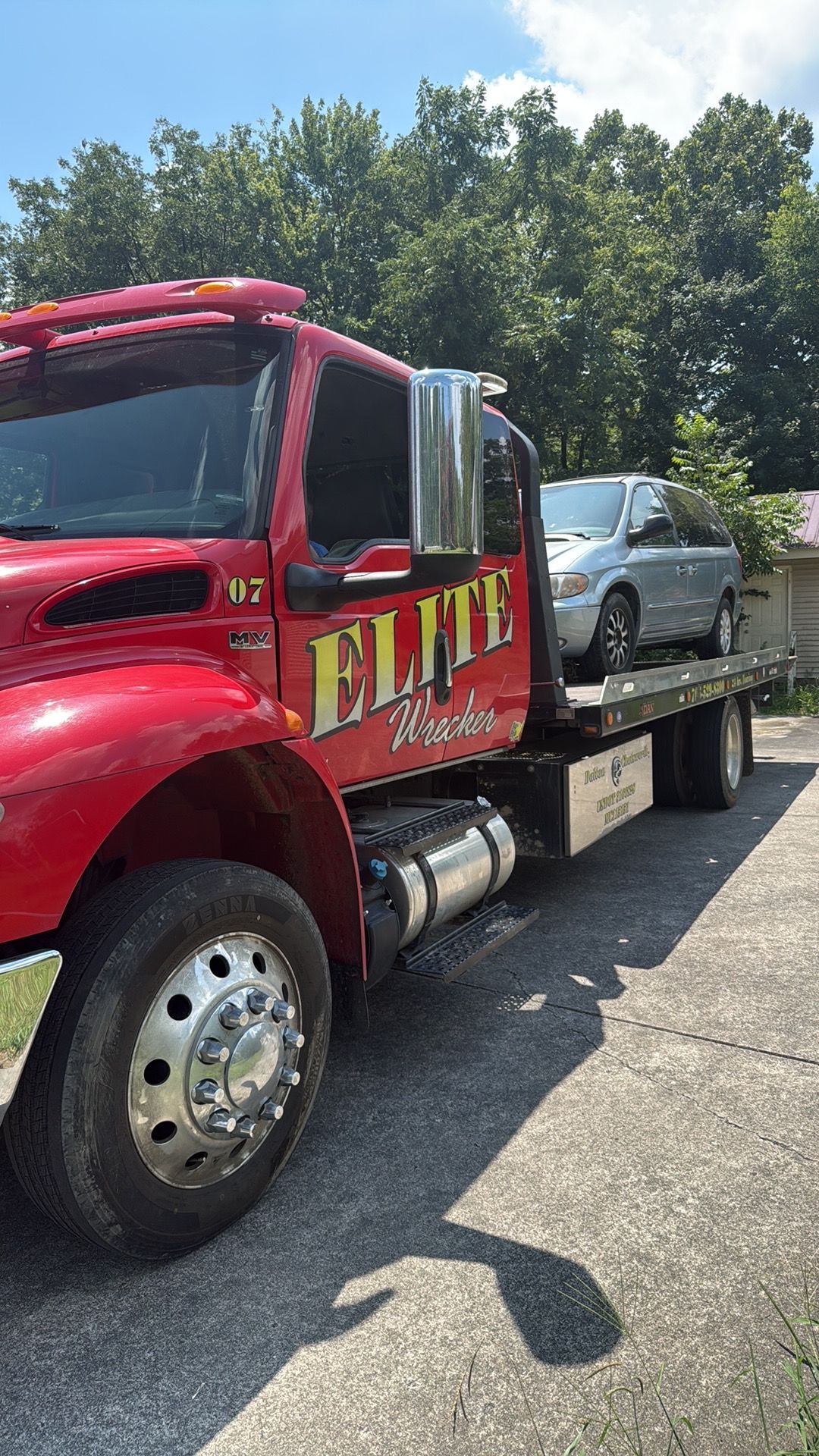 Red tow truck carrying a silver car on a flatbed in a sunny lot