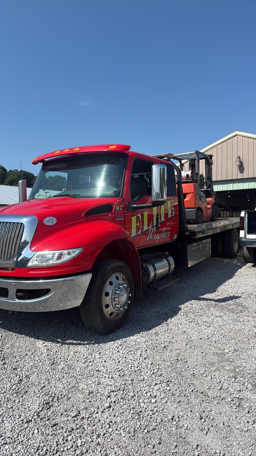 Red flatbed tow truck parked on gravel under a clear blue sky