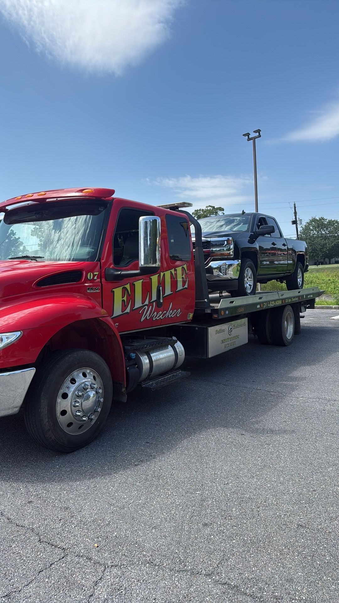 Red tow truck carrying a damaged dark SUV on its flatbed under a blue sky