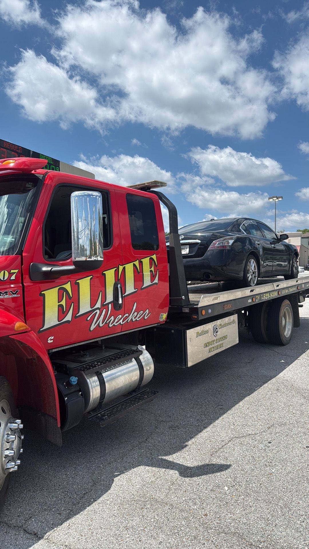 Red flatbed tow truck carrying a black car under a cloudy sky