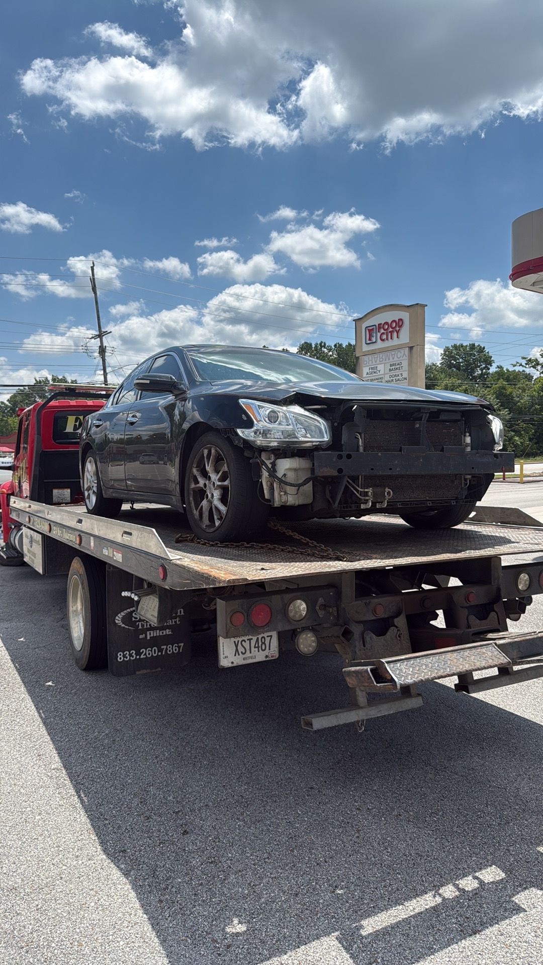 Black sedan on a tow truck in a parking lot under a partly cloudy sky
