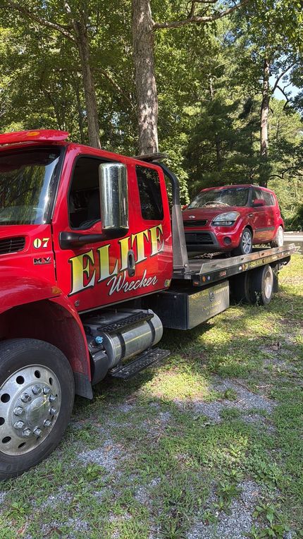 Red tow truck carrying a red SUV on a flatbed in a wooded area