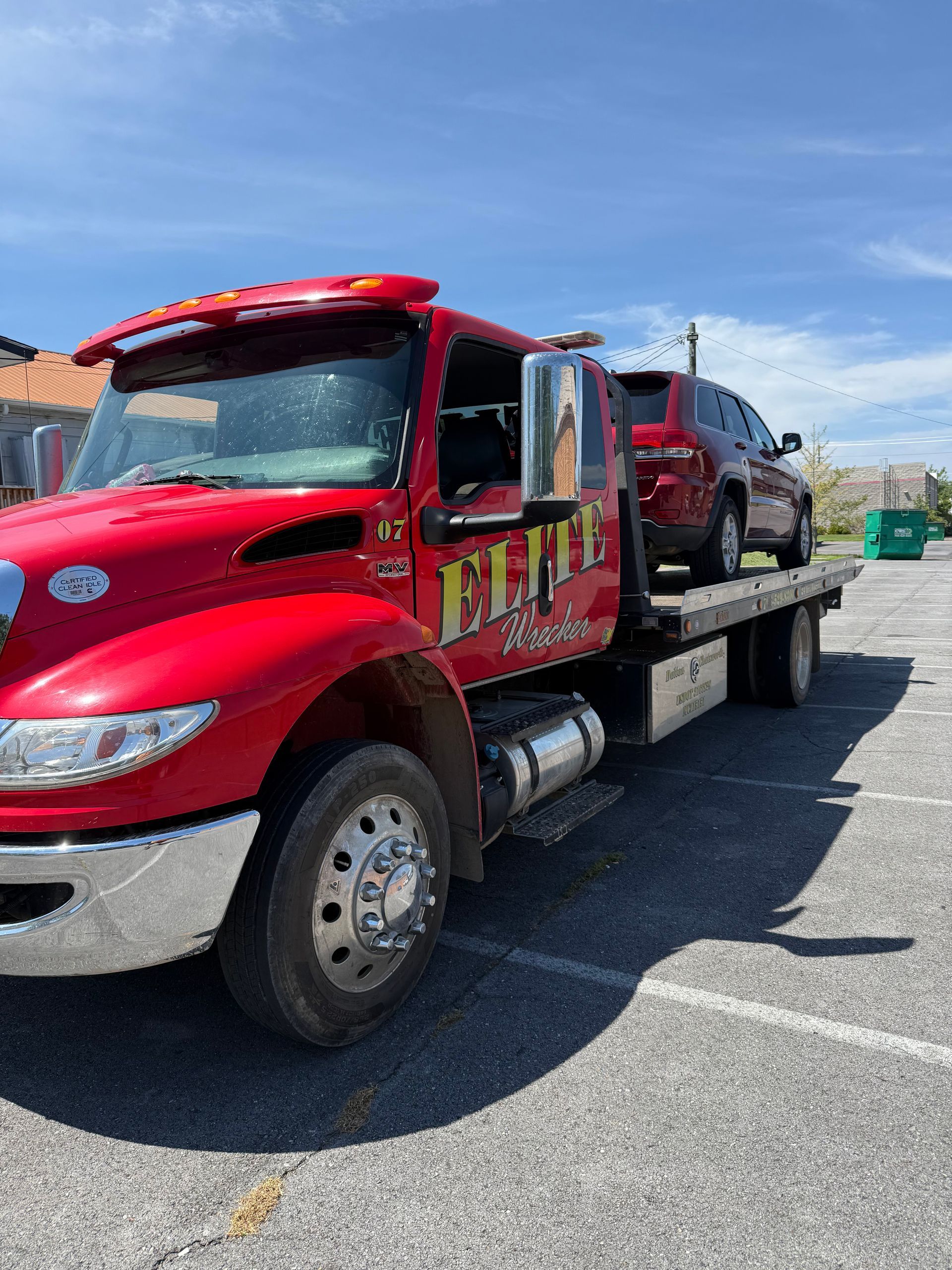 Red tow truck carrying a maroon SUV parked on a sunny street