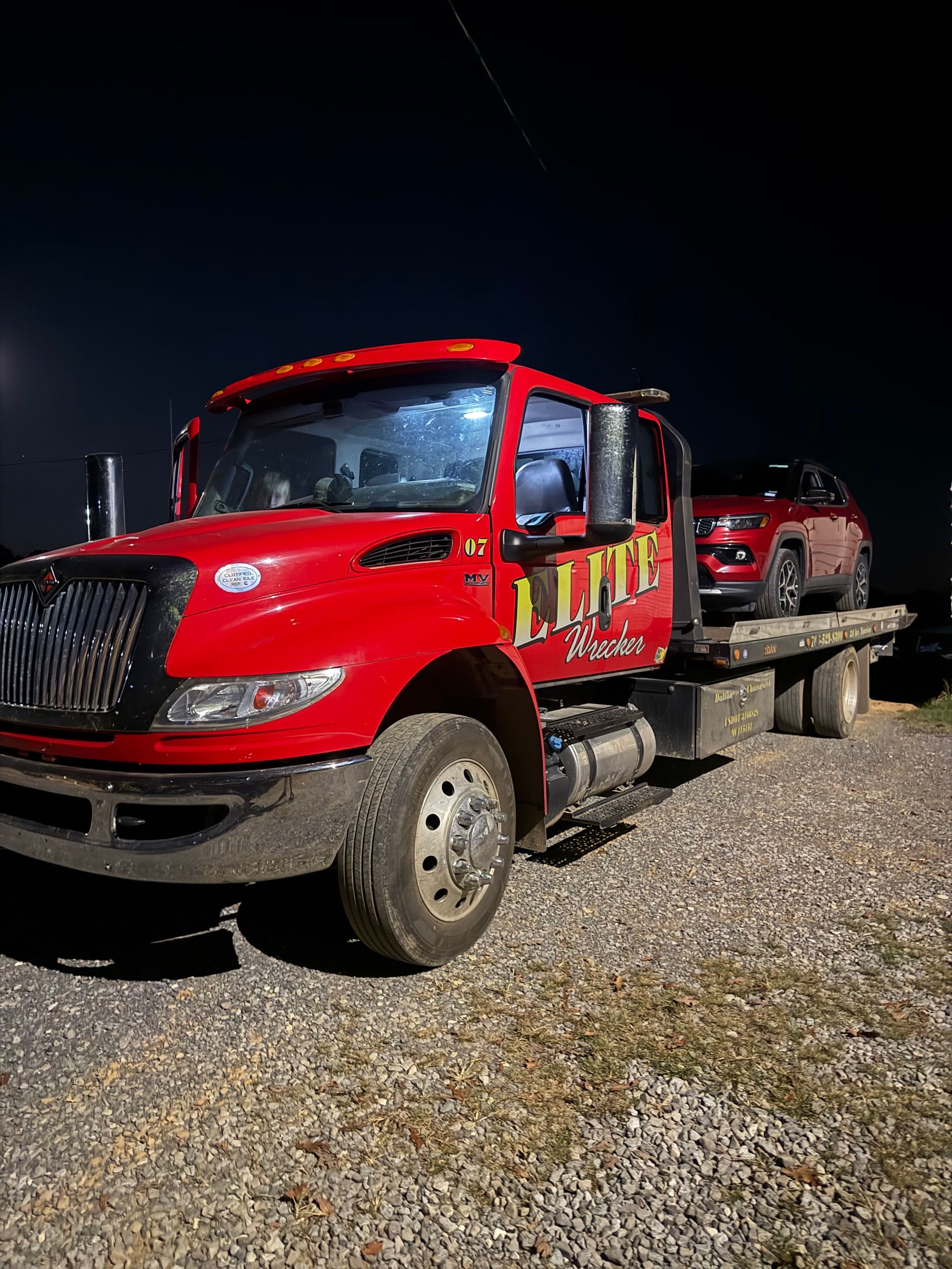 Red tow truck on gravel at night, with a pickup loaded on the flatbed trailer.