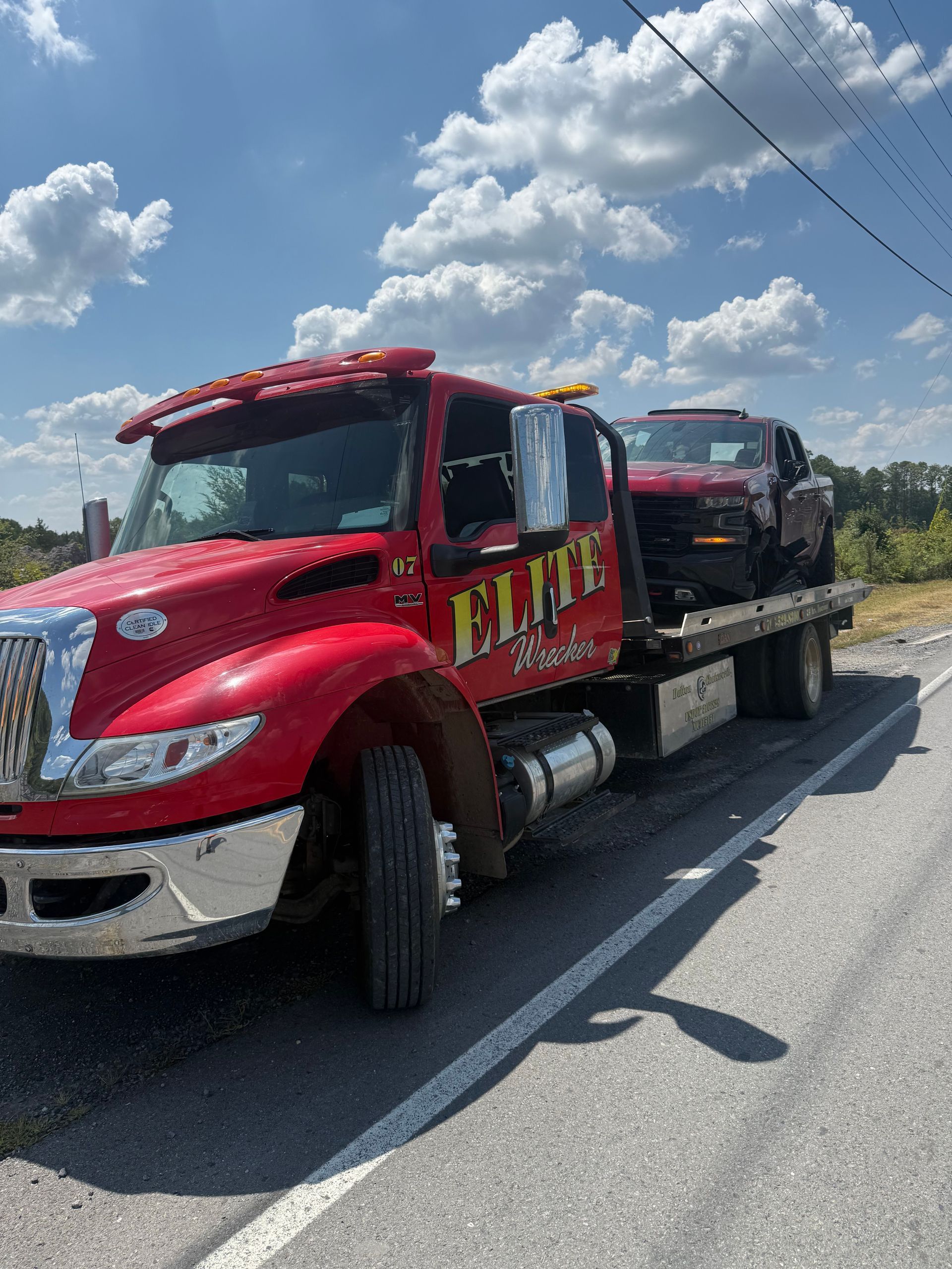 Red tow truck hauling a black SUV on a roadside under a blue sky