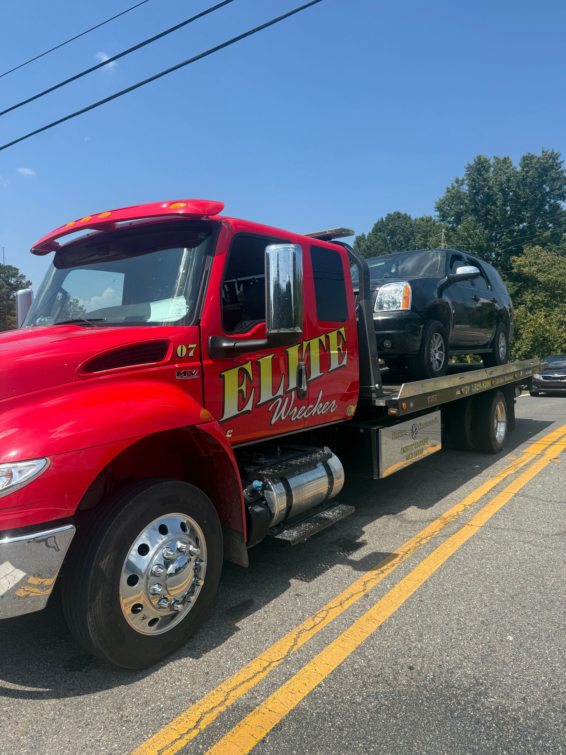 Red tow truck carrying a black SUV on a roadside under a clear blue sky.