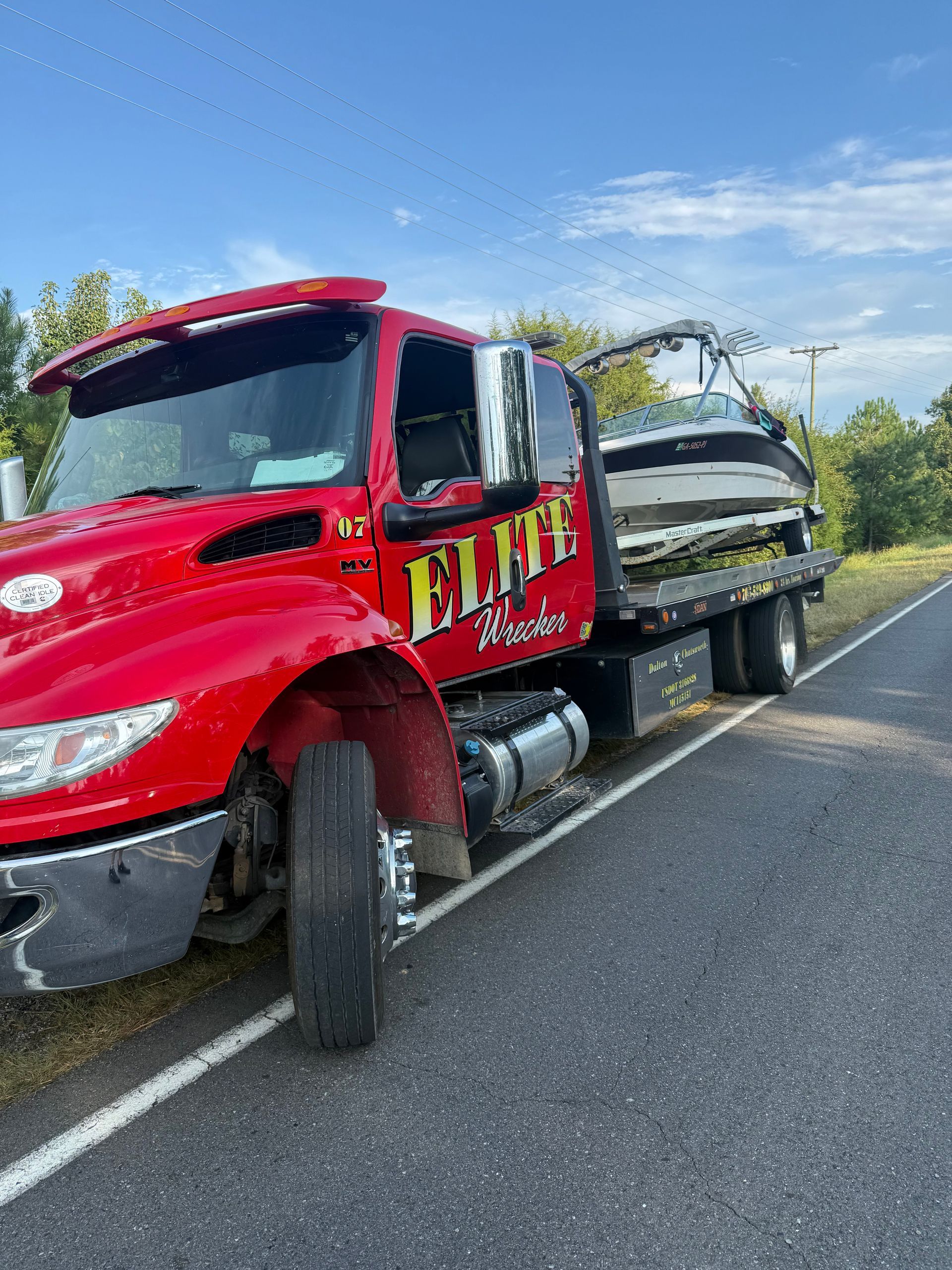 Red tow truck hauling a white boat trailer along a roadside under a blue sky