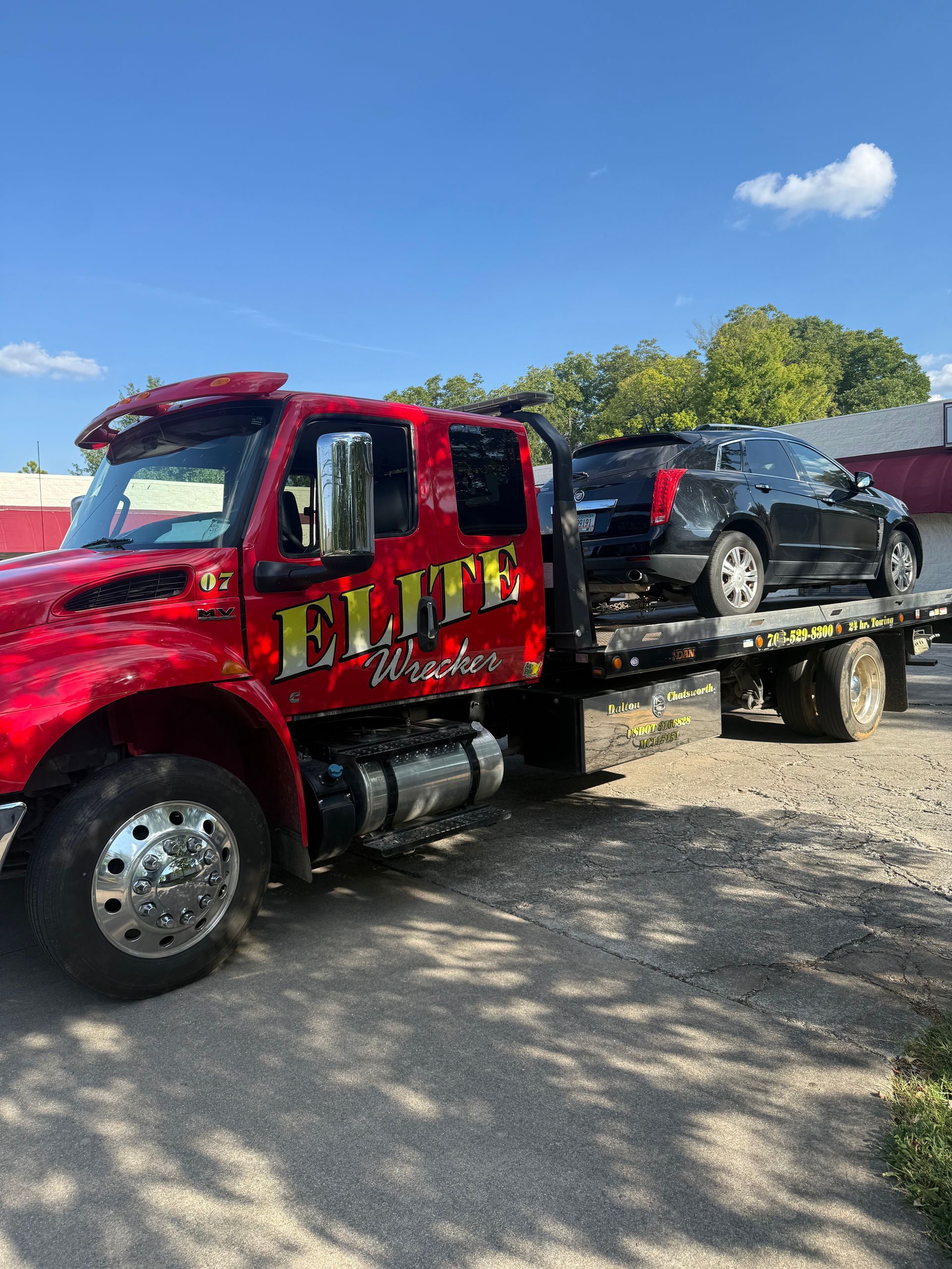 Red tow truck hauling a black car on a flatbed under a blue sky.