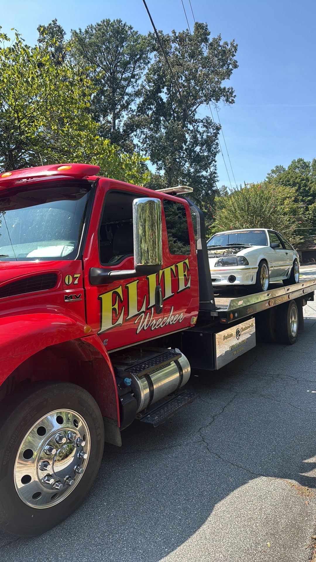 Red tow truck hauling a white car on a flatbed in a sunny parking lot