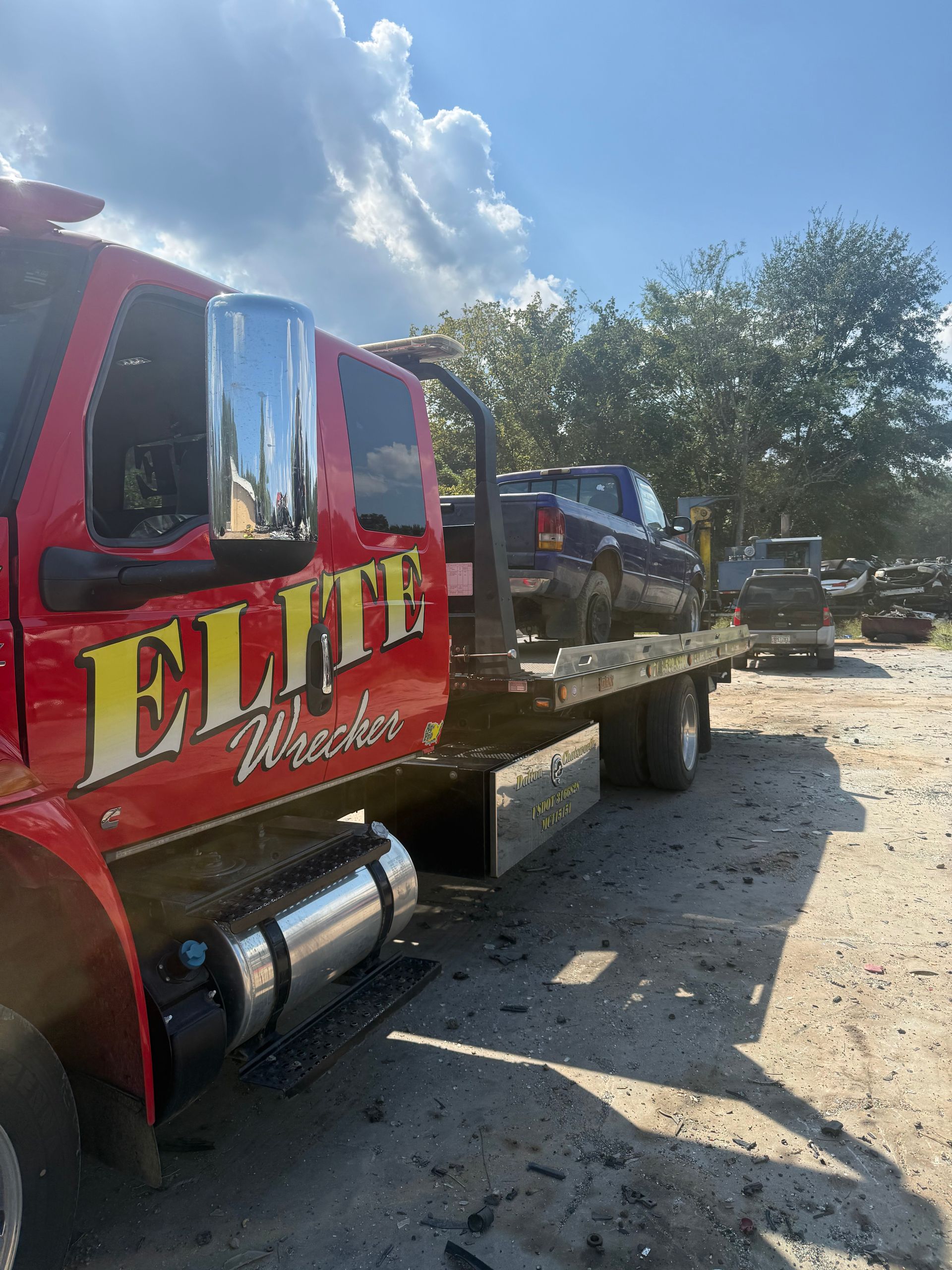 Red tow truck hauling a black car on a flatbed in a sunny outdoor lot