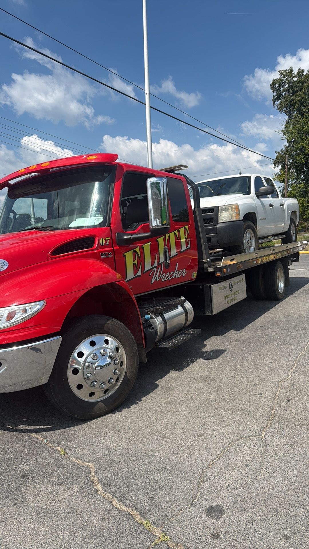 Red tow truck carrying a silver SUV on a flatbed under a blue sky