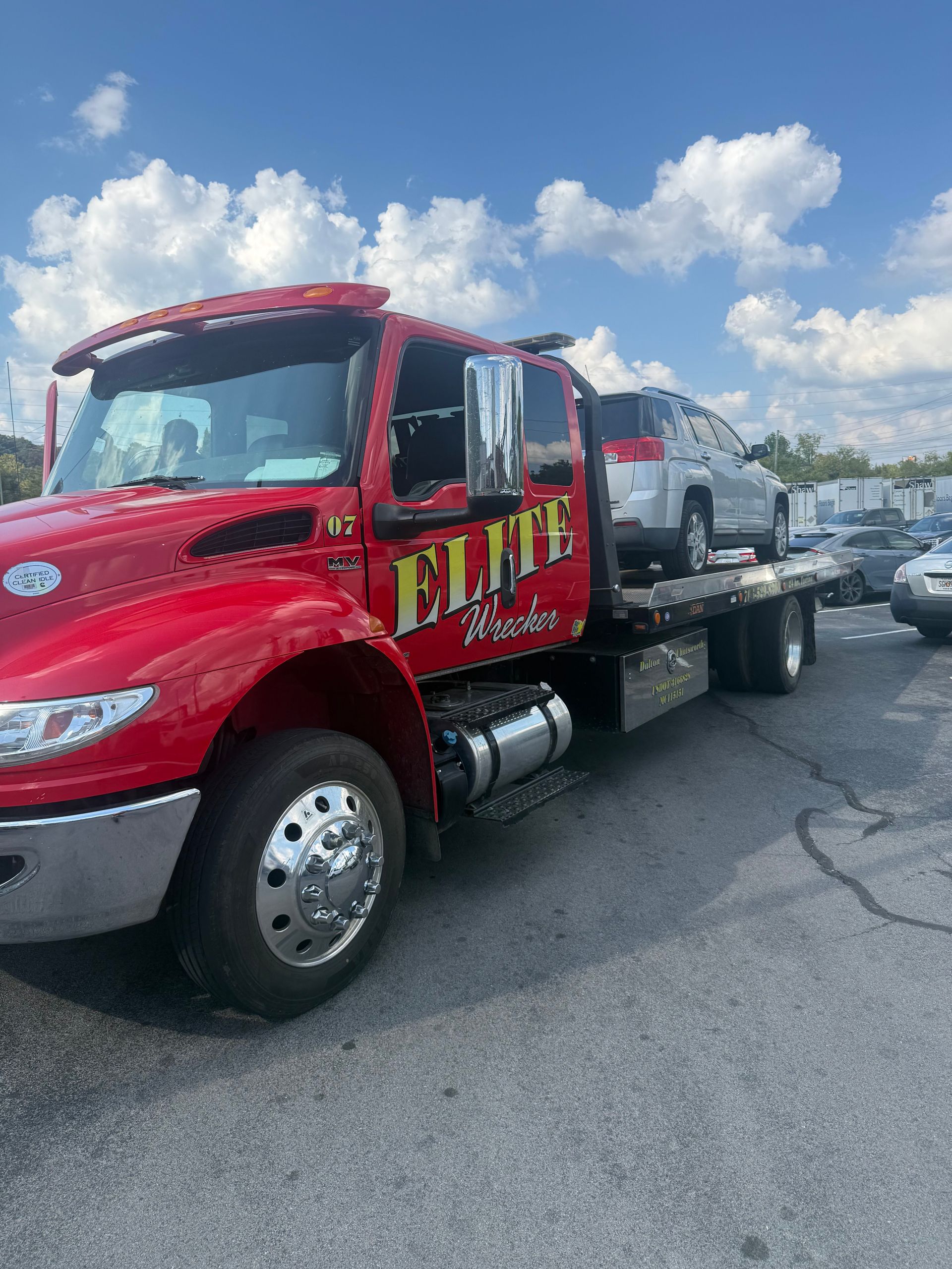 Red Elite tow truck hauling a white vehicle on a sunny roadside under a blue sky