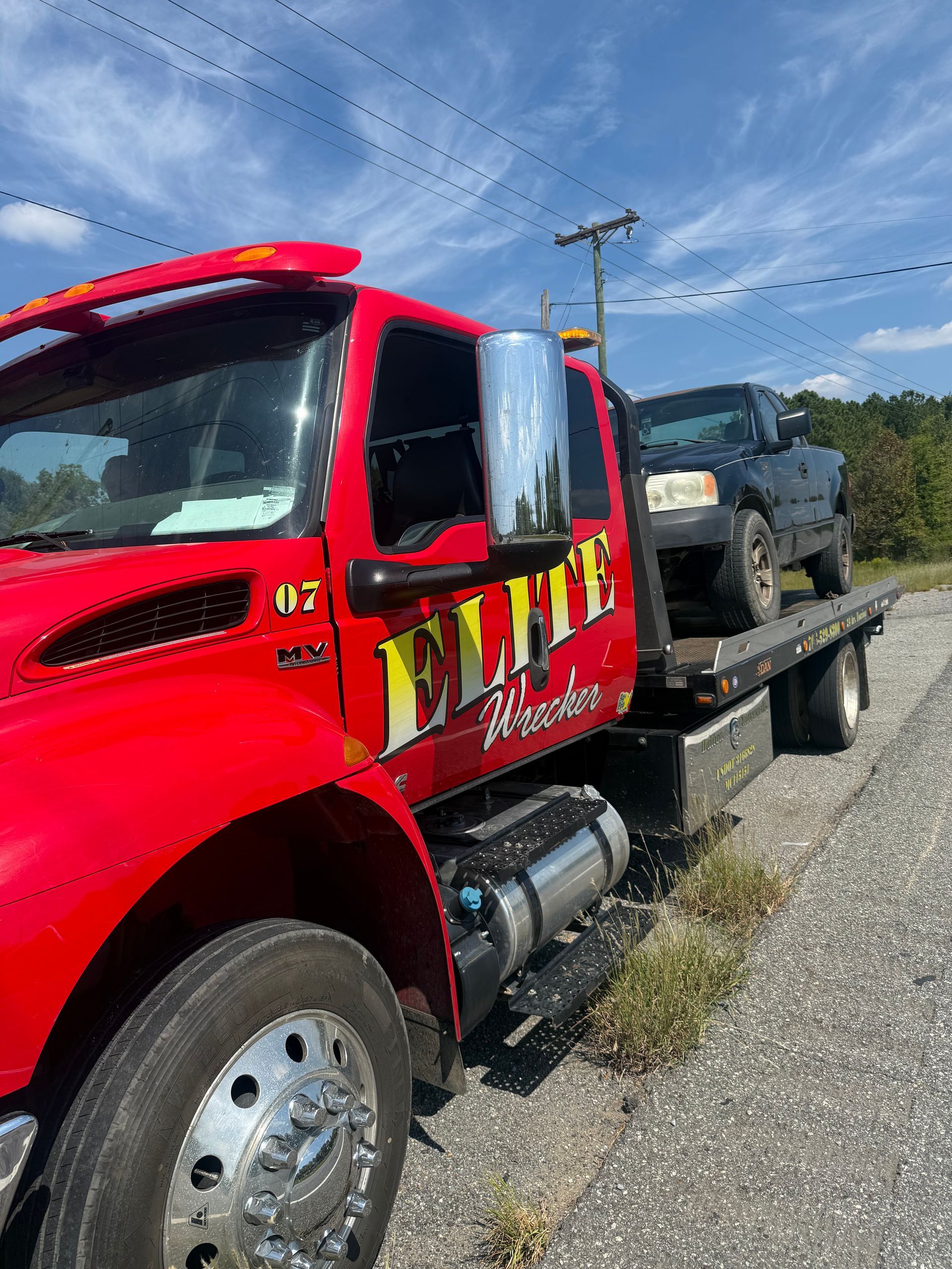 Red tow truck hauling a black pickup on a flatbed under a blue sky
