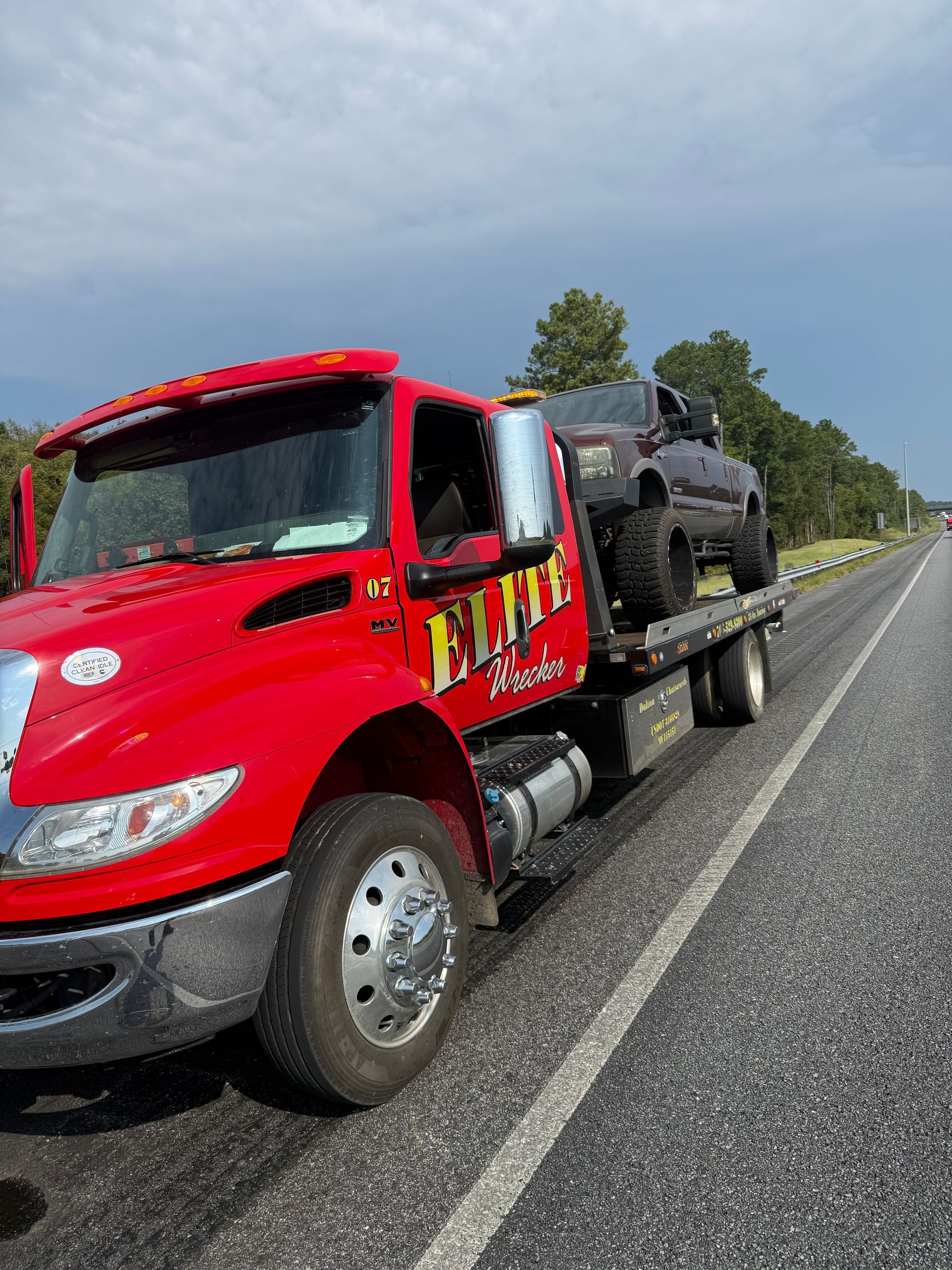 Red tow truck hauling a black SUV on a highway shoulder under a cloudy sky