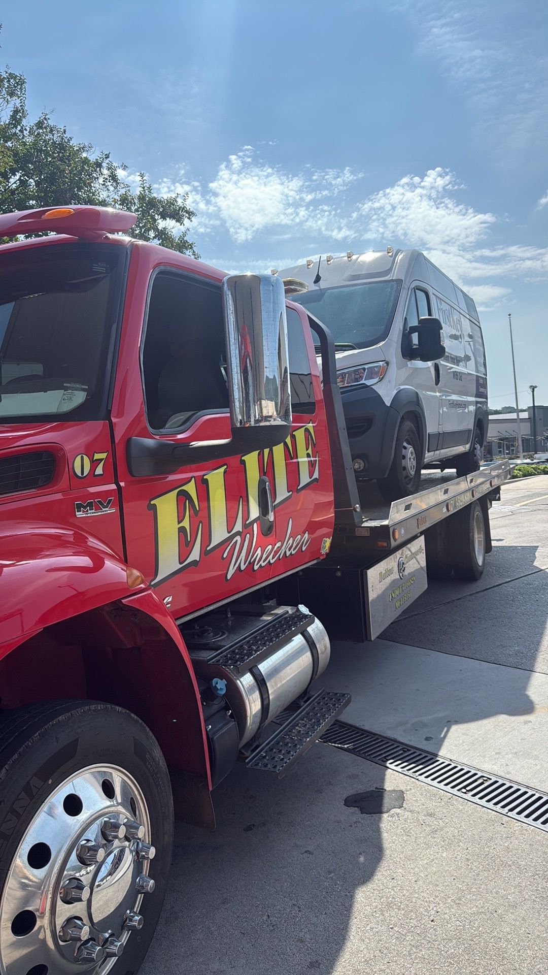 Red tow truck hauling a silver SUV on a flatbed under a bright blue sky