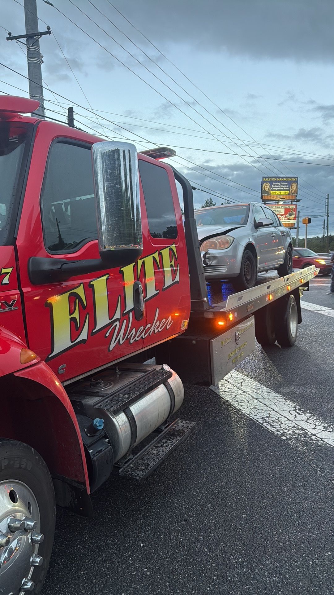 Red tow truck hauling a silver car on a wet highway in rainy weather