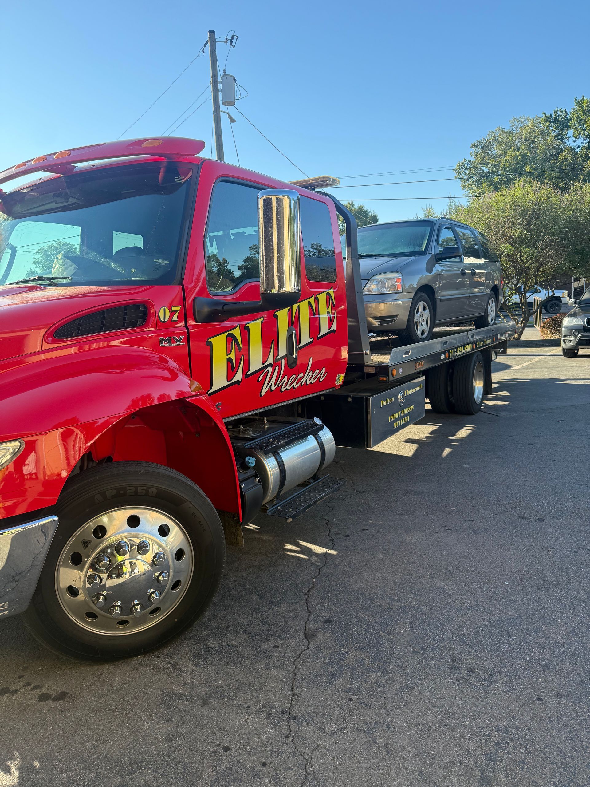 Red tow truck hauling a gray SUV on a sunny street.