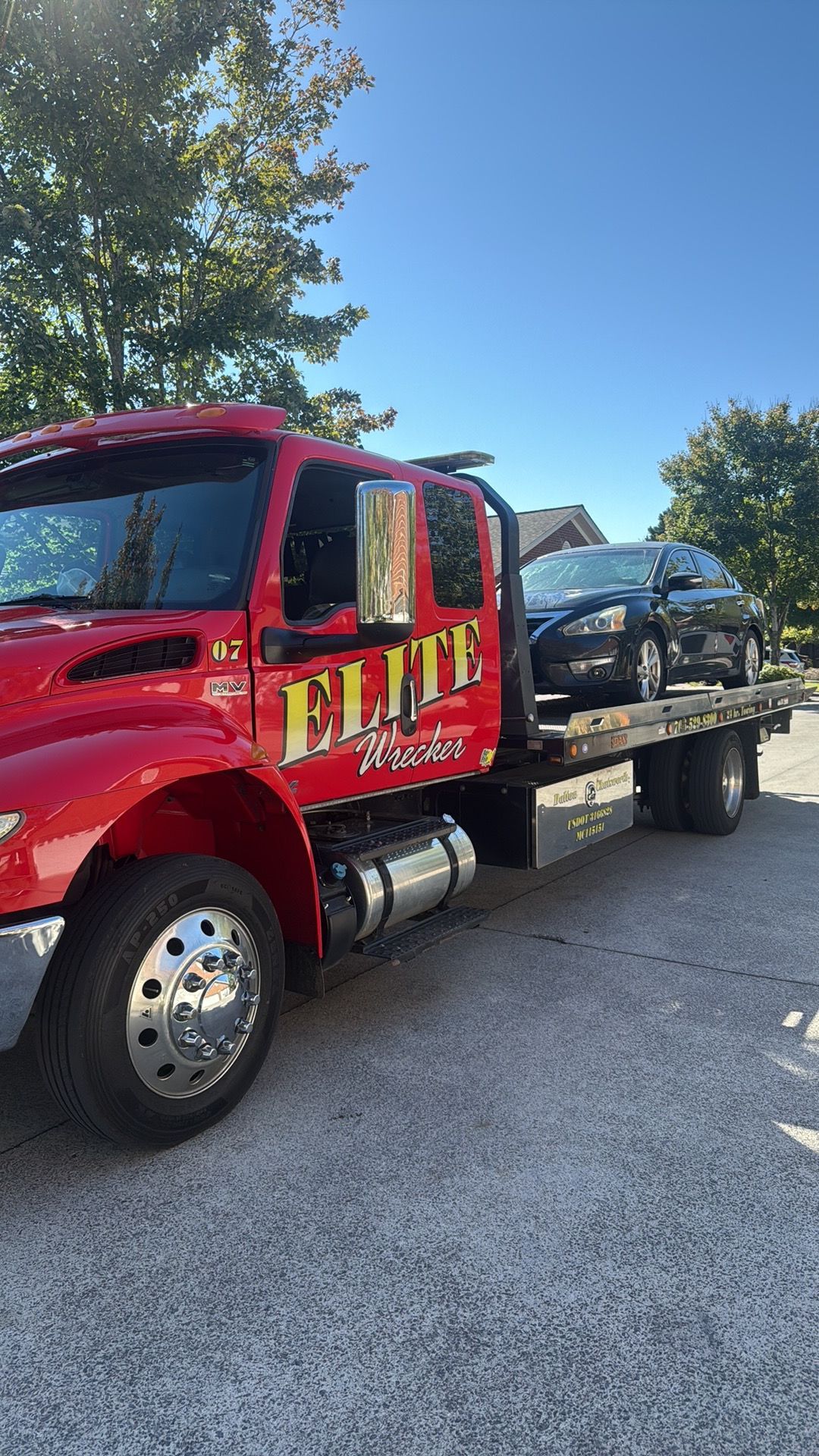 Red tow truck loaded with a black SUV parked on a gravel roadside under a blue sky